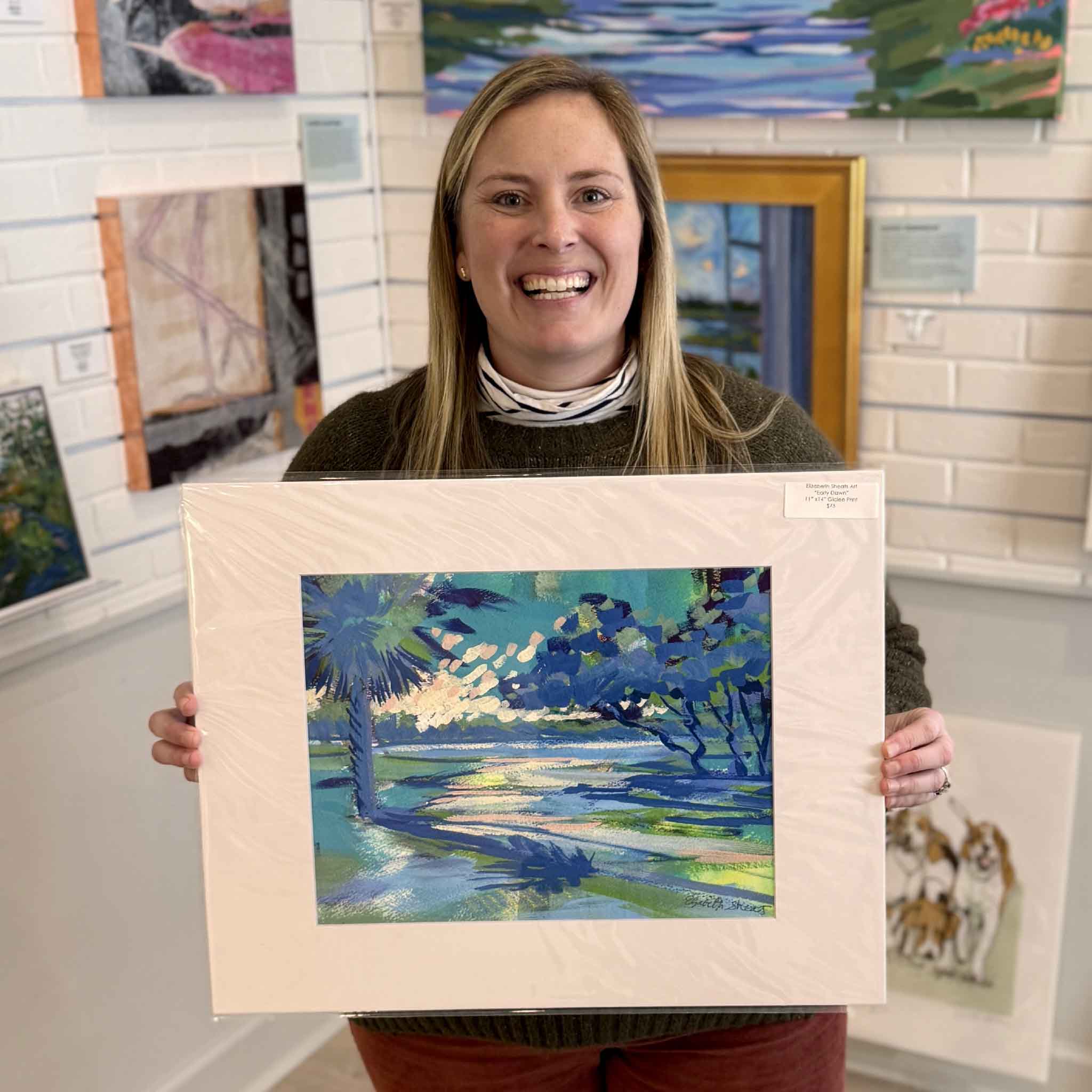Bordy of Gray Man Gallery holding the 16x20 matted version of “Early Dawn” by Elizabeth Sheats, a coastal Lowcountry sunrise giclée print with vibrant blue and green tones, showcasing size, archival matting, and gallery presentation in Pawleys Island South Carolina