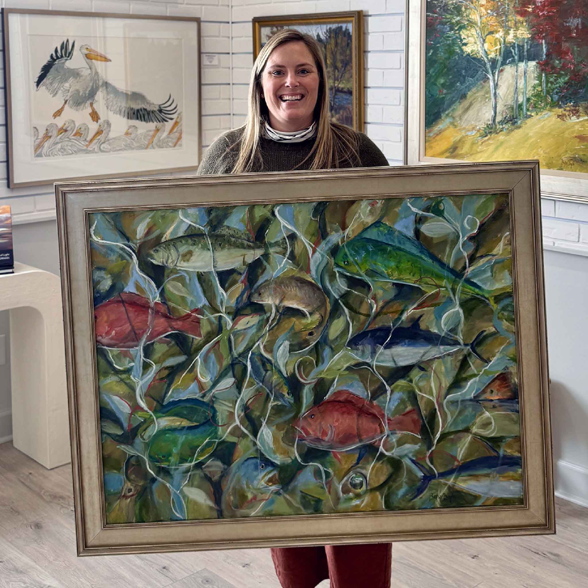 Gray Man Gallery staff member Bordy holding “Fishing Lines Galore,” a large original painting by local artist Betsy Boyle at Gray Man Gallery in Pawleys Island, South Carolina, showcasing contemporary coastal marsh fish imagery and expert custom framing