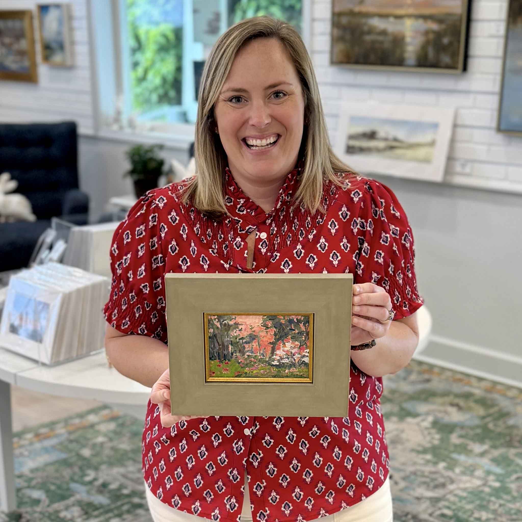 Bordy holding Garden at Dusk by Jeanne O’Neal original oil painting created at Brookgreen Gardens inside Gray Man Gallery Pawleys Island showing scale of framed floral landscape with glowing pink sky
