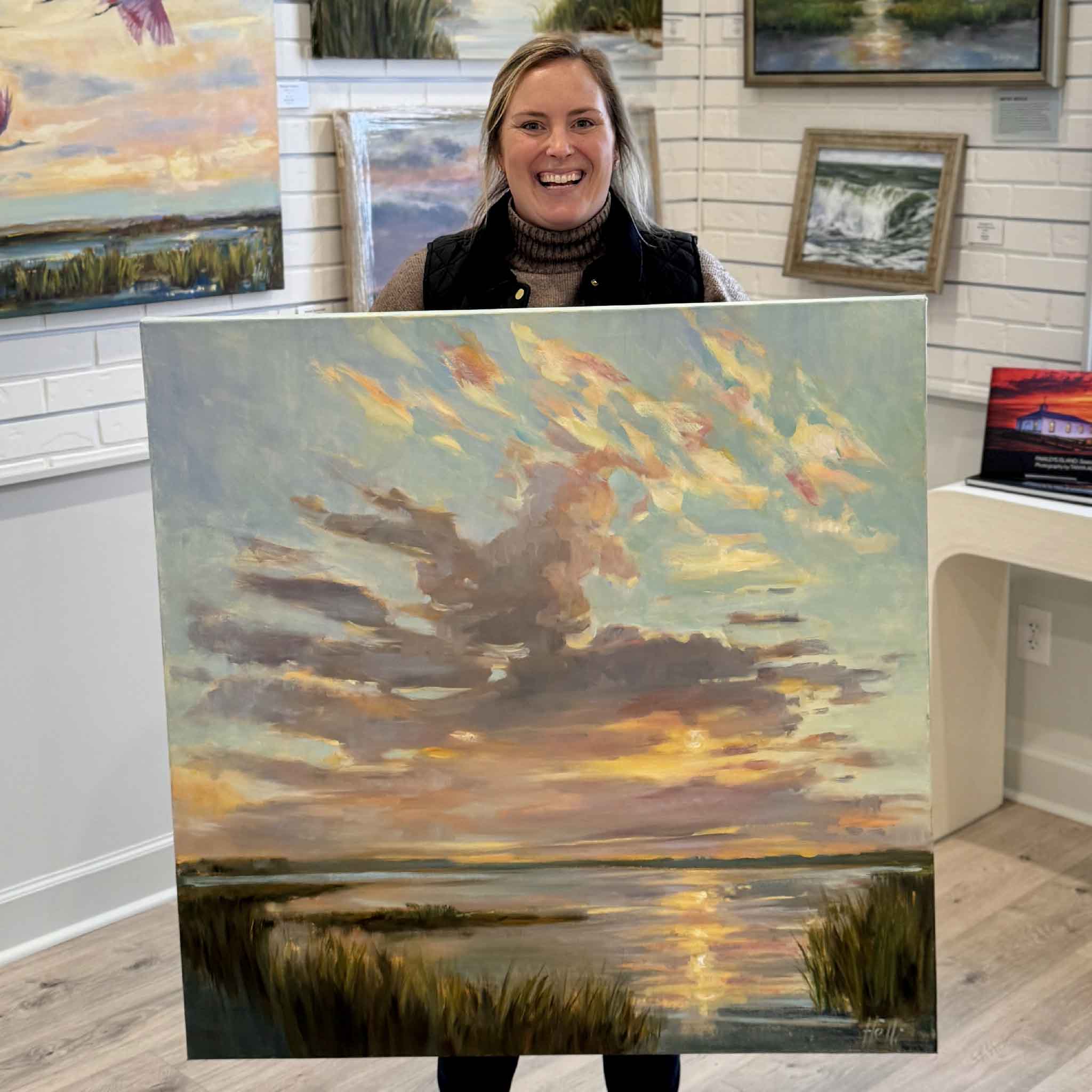 Gray Man Gallery staff member Bordy holding “Morning Show,” a large original coastal sunrise painting by local artist Helli Luck at Gray Man Gallery in Pawleys Island, South Carolina, featuring Lowcountry marsh landscape artwork and expert custom framing
