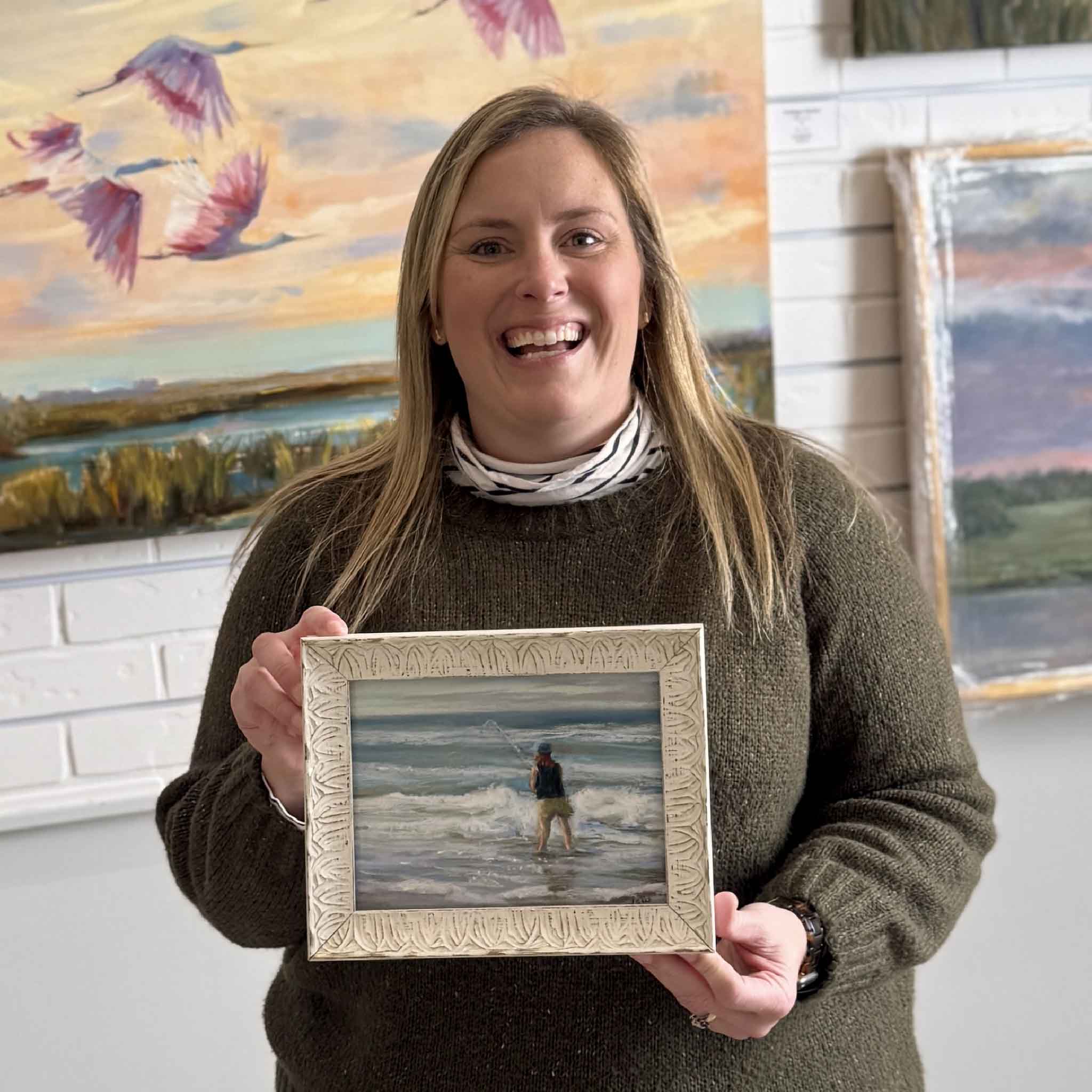 Gray Man Gallery team member Bordy holding the framed pastel artwork Surf Casting by local artist Joanne Willoughby inside the Pawleys Island gallery showcasing local coastal art