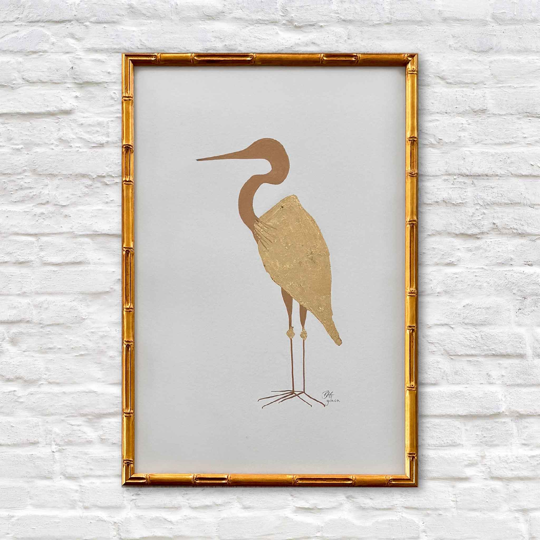 Braden Grafe original mixed media artwork Goldie featuring a minimal heron silhouette with gold leaf body on a soft neutral background, framed in a warm bamboo style frame at Gray Man Gallery in Pawleys Island showcasing refined Lowcountry coastal art