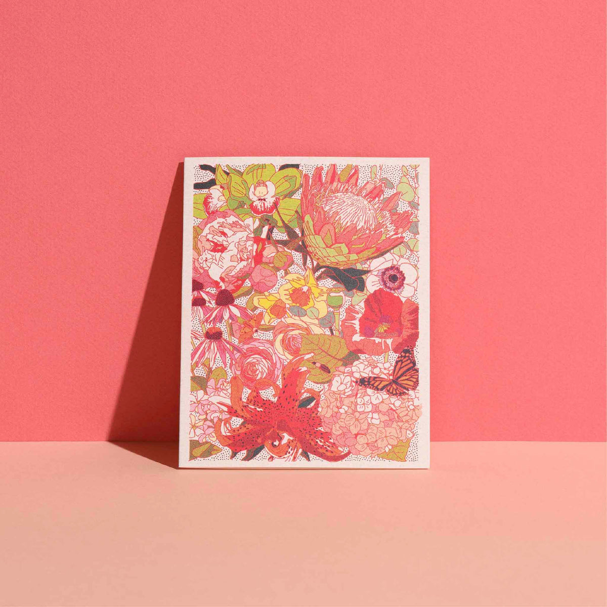 Colorful Wild Florals notecard from the Caroline Clark boxed stationery set, featuring intricate protea, lilies, poppies, hydrangeas, roses, coneflowers and a butterfly in shades of coral, pink, green and yellow, photographed against a bright coral background for Gray Man Gallery in Pawleys Island, South Carolina.
