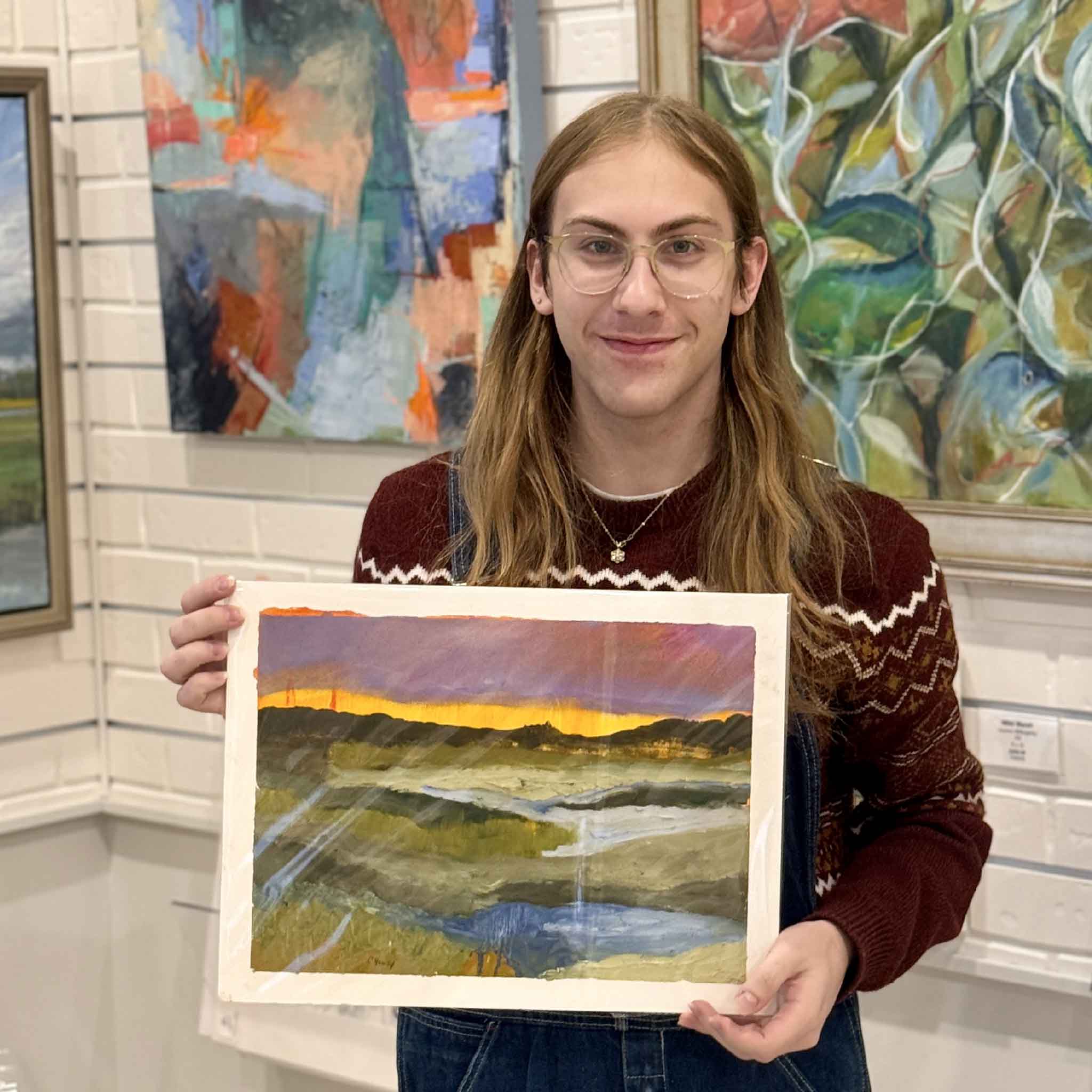 This image shows a Gray Man Gallery employee holding Caroline Young's 16x12 Twilight Over Marsh  inside Gray Man Gallery, highlighting its vibrant coastal colors and its convenient fit for a standard 12x16 frame.