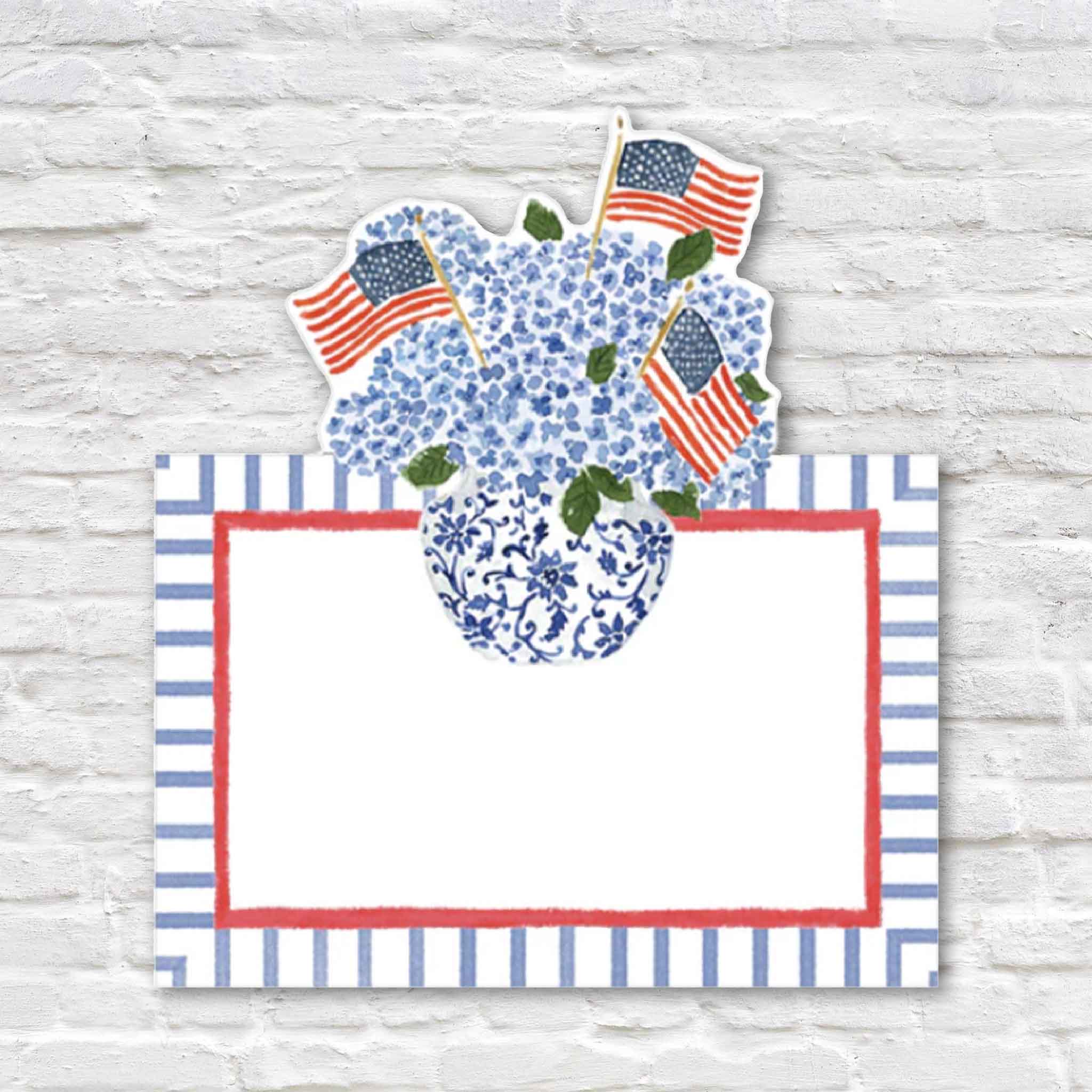 Caspari Flags & Hydrangeas die-cut place cards featuring artwork by Lindsay Brackeen, with blue hydrangeas arranged in a chinoiserie-inspired vase accented by American flags. These premium tented place cards are sold in a set of eight at Gray Man Gallery in Pawleys Island, South Carolina, and are perfect for Fourth of July celebrations, Memorial Day, patriotic entertaining, weddings, dinner parties, and elegant coastal table settings.