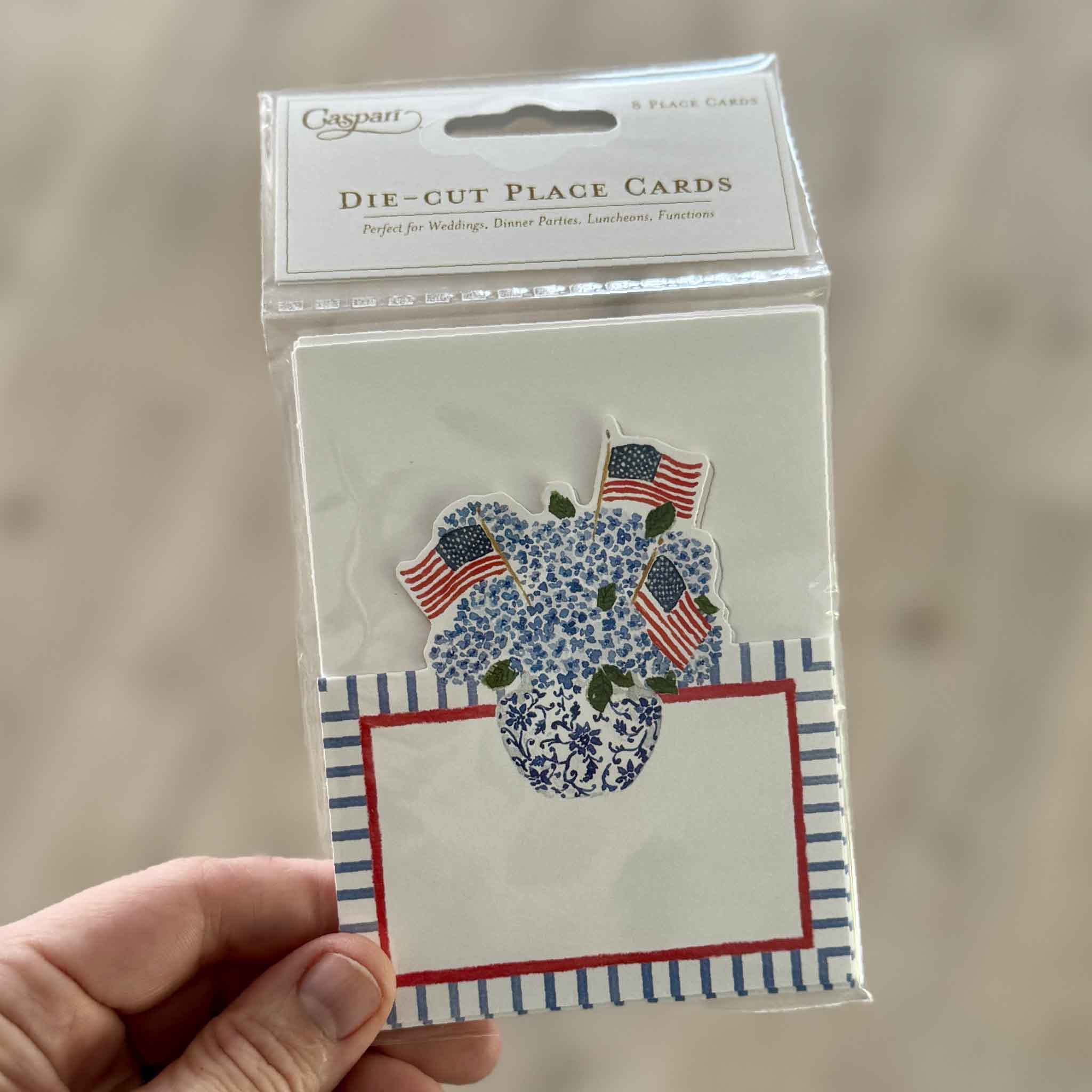 Packaged set of eight Caspari Flags & Hydrangeas die-cut place cards featuring artwork by Lindsay Brackeen, photographed at Gray Man Gallery in Pawleys Island, South Carolina. The premium cardstock place cards feature blue hydrangeas in a decorative blue-and-white vase with American flags and are ideal for patriotic entertaining, weddings, holiday gatherings, and coastal table décor.
