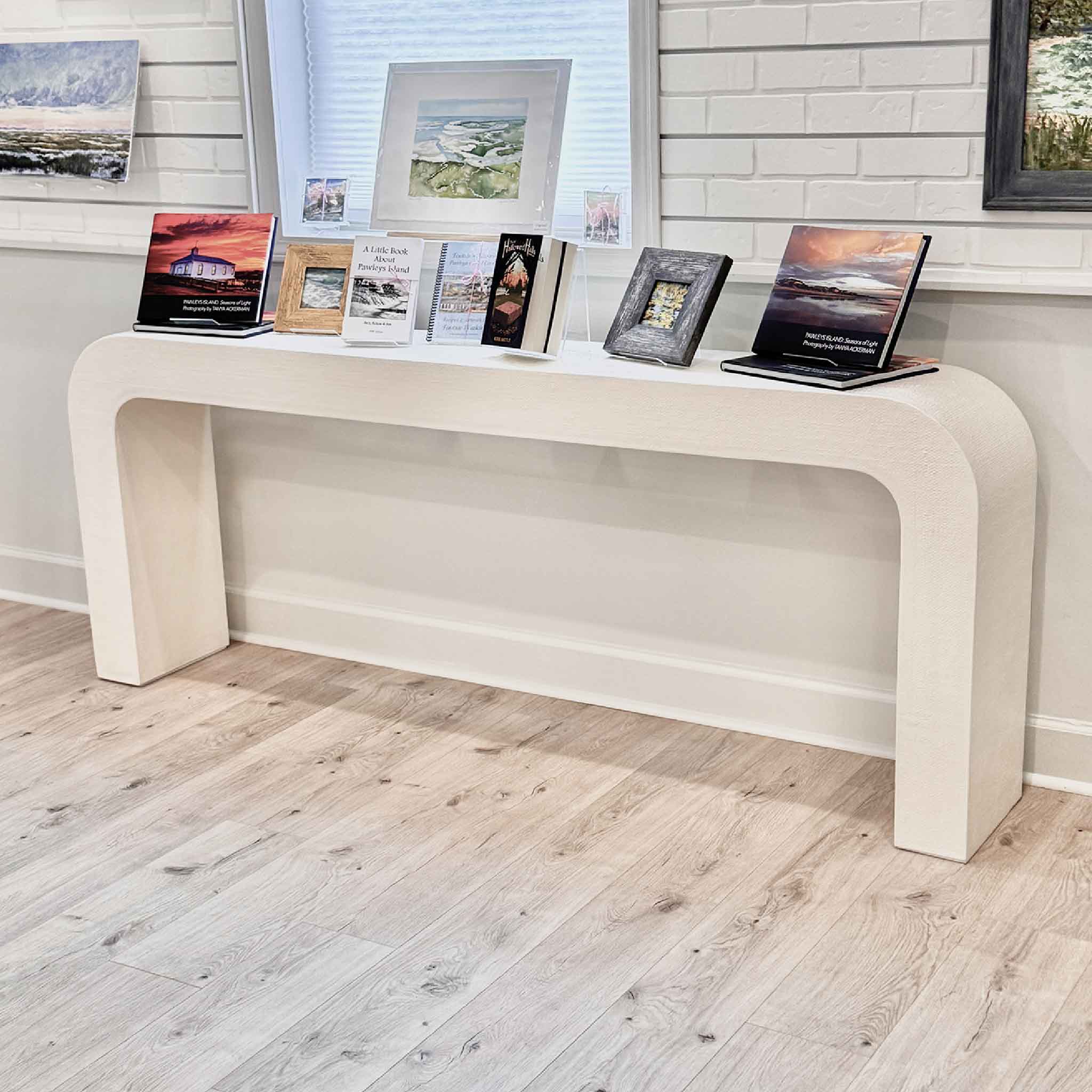 CB2 Crescent ivory resin console table displayed inside Gray Man Gallery Pawleys Island styled with local art books and framed artwork showing scale texture and waterfall silhouette of pre owned designer console table available for local pickup
