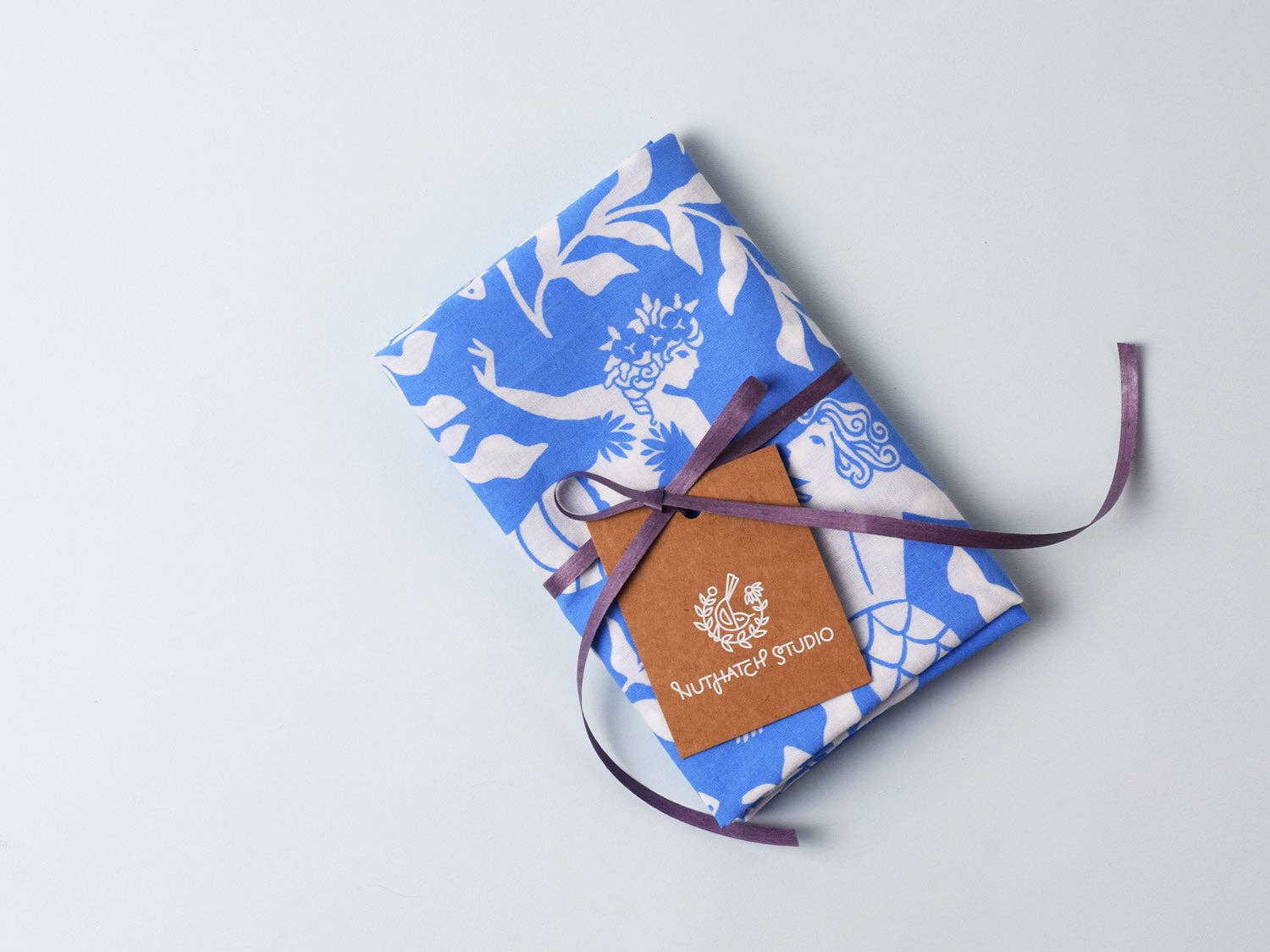 Cerulean Mermaid organic cotton bandana by Chrissie Van Hoever folded and tied with ribbon in its gift-ready packaging. This sustainable textile makes a thoughtful coastal gift from Gray Man Gallery in Pawleys Island, South Carolina.