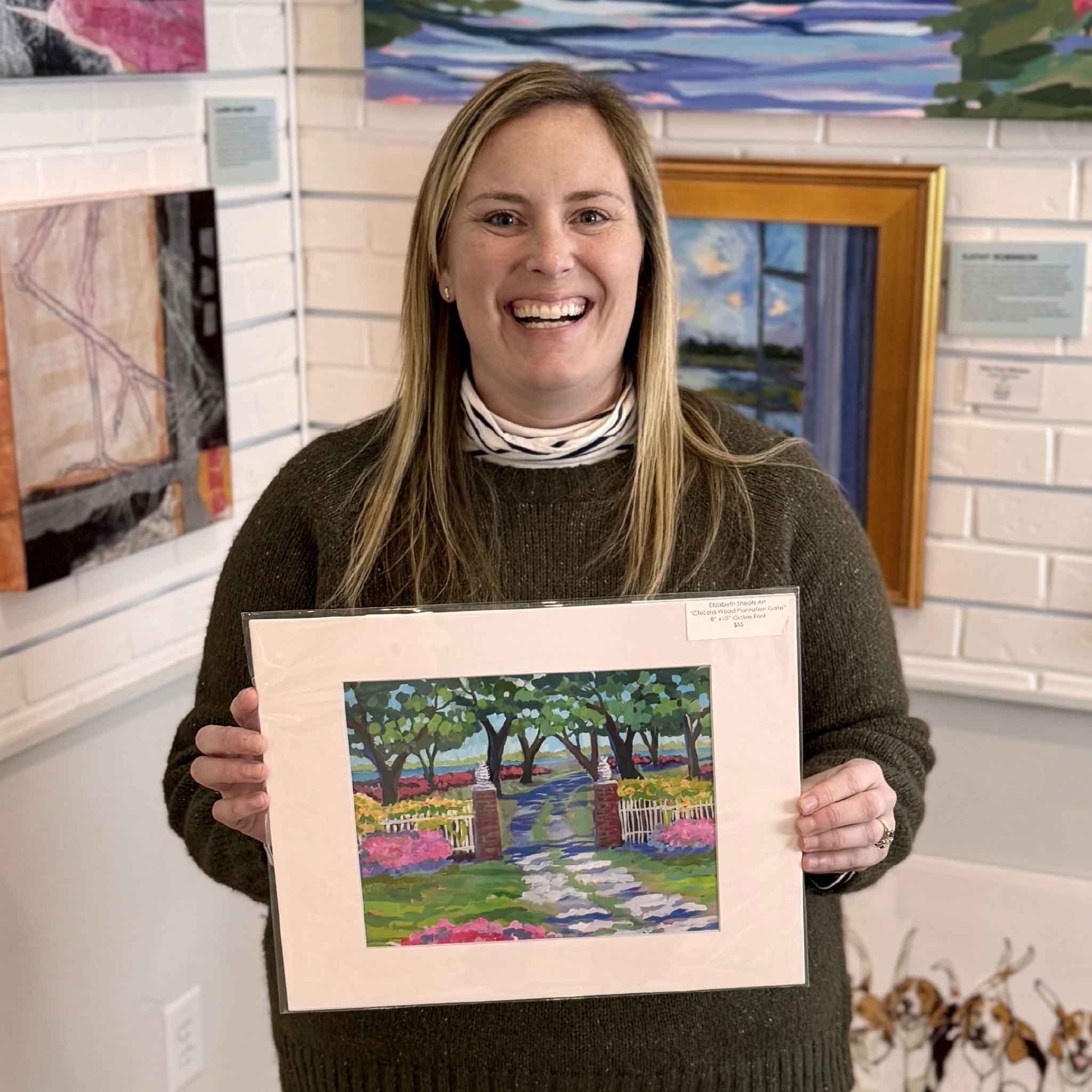 Bordy holding Elizabeth Sheats 11x14 Chicora Wood Plantation Gate Lowcountry fine art giclée print inside Gray Man Gallery in Pawleys Island South Carolina, historic plantation entrance with live oak trees, brick gateposts, garden pathway, azaleas, and Southern coastal landscape artwork
