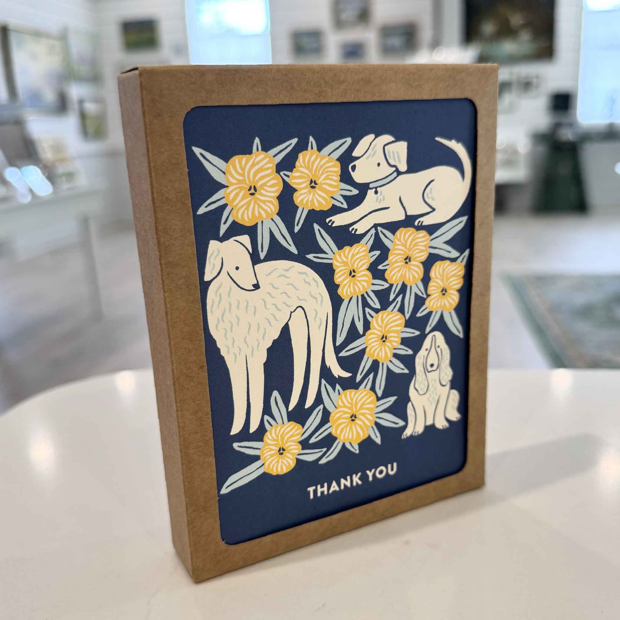 Nuthatch Studio Dogs All-Occasion Greeting Card Boxed Set displayed inside Gray Man Gallery in Pawleys Island, South Carolina. This eco-friendly boxed set includes eight assorted dog-themed greeting cards with original illustrations by Chrissie Van Hoever, featuring thank you, thinking of you, birthday, and congratulations designs printed on premium 100% recycled paper with matching recycled kraft envelopes.