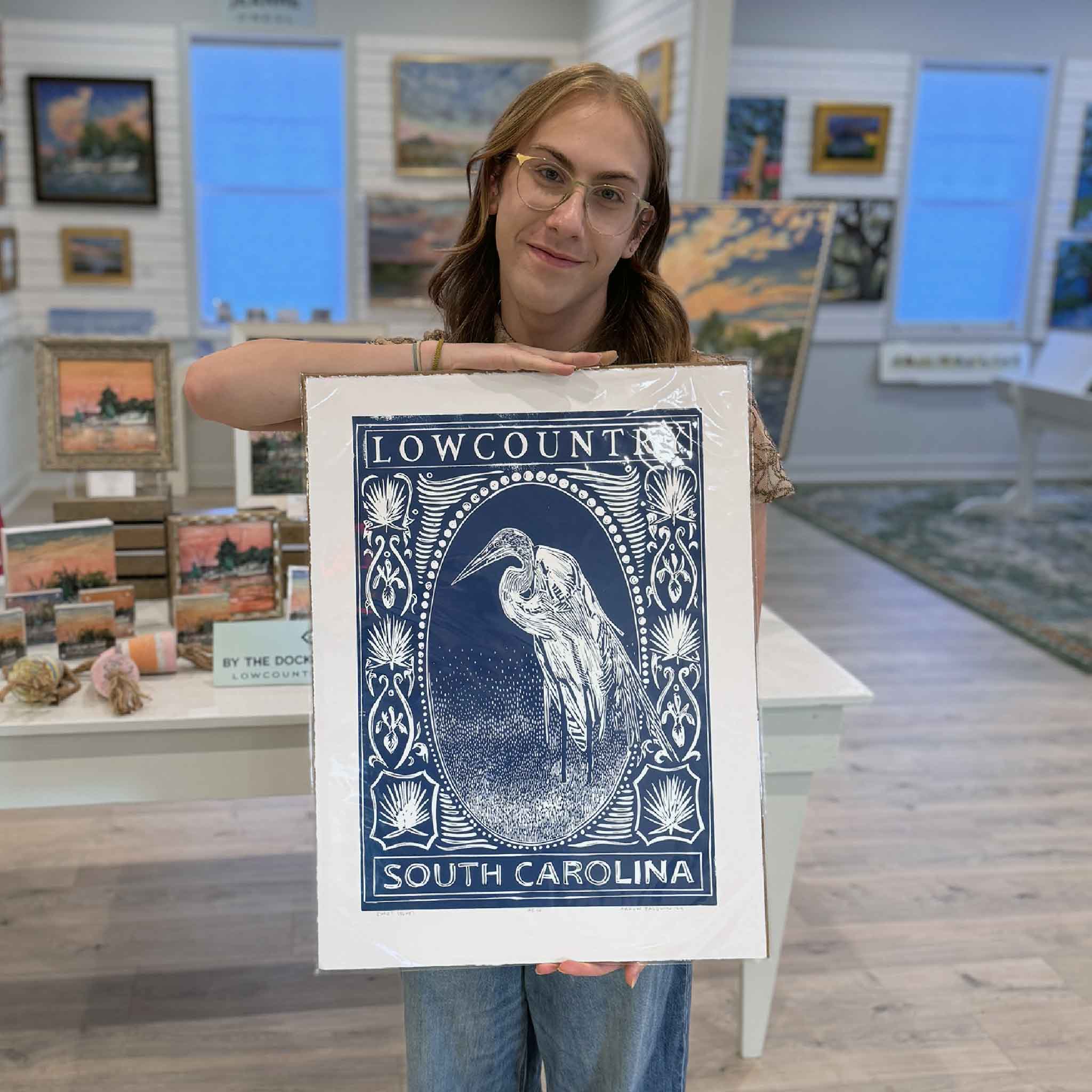 Alex holding the blue Egret linocut print by Aaron Baldwin inside Gray Man Gallery.