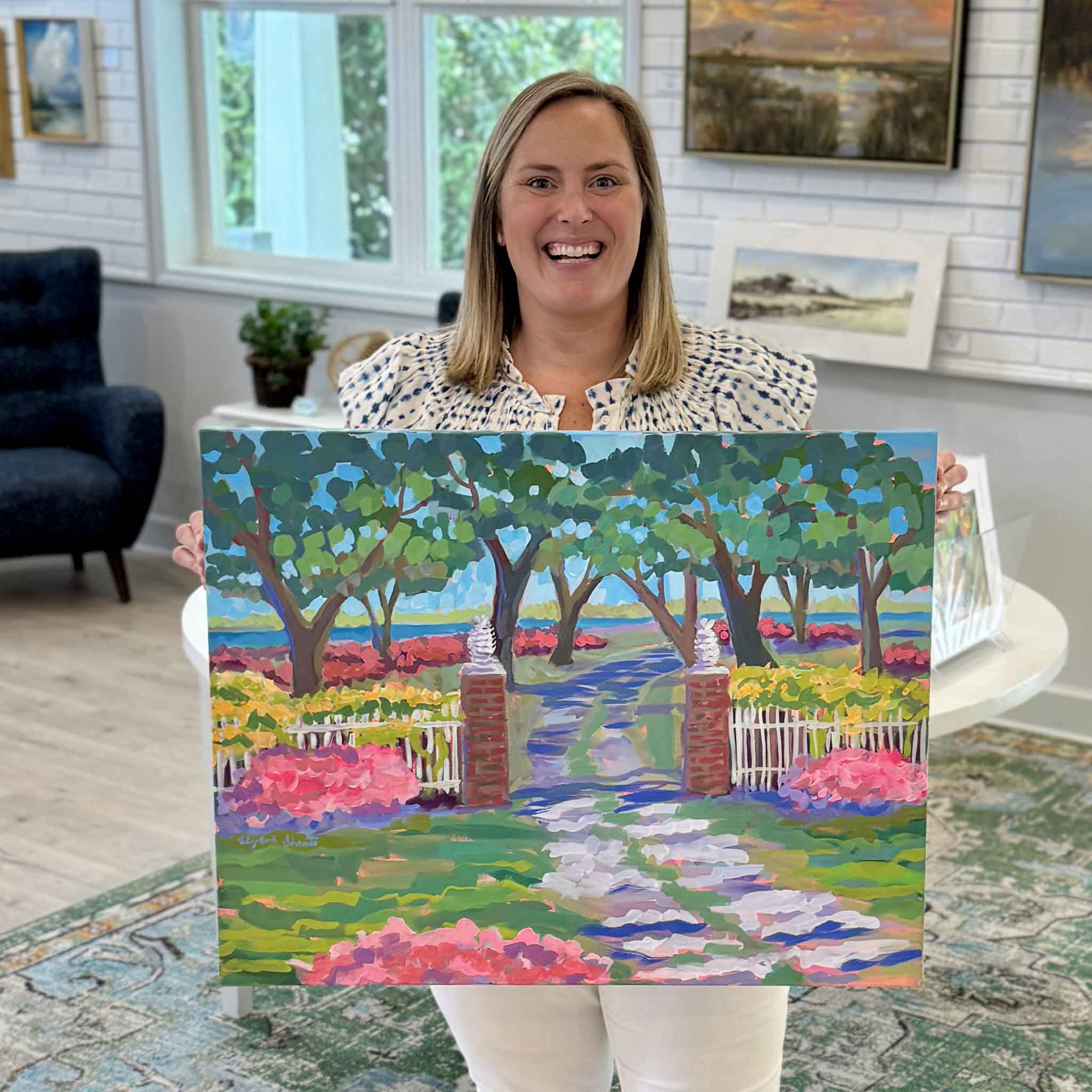 Bordy holding Chicora Wood Plantation Gate acrylic painting by Elizabeth Sheats inside Gray Man Gallery in Pawleys Island showing scale with colorful azaleas, white fence, and historic Georgetown plantation entrance