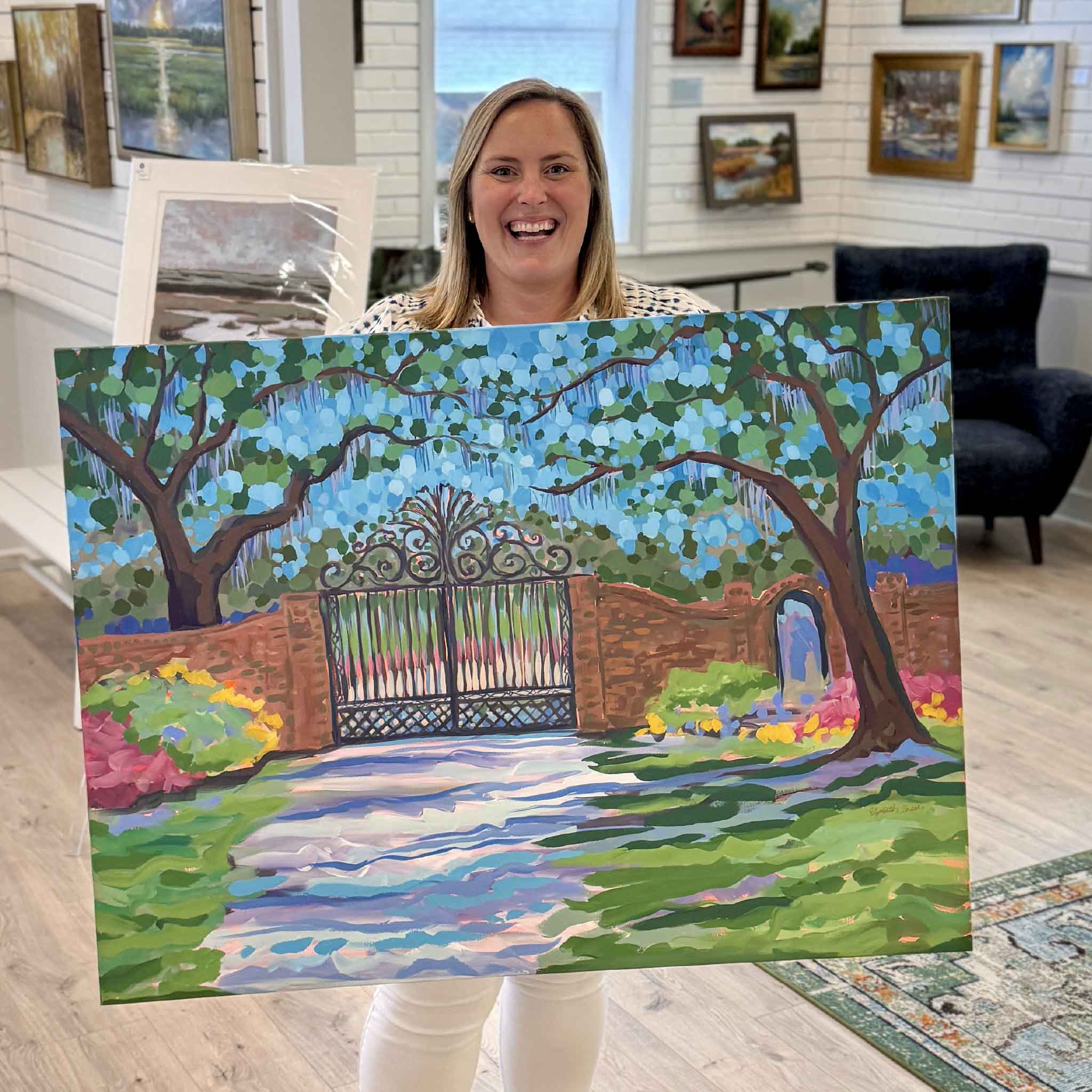 Bordy holding Litchfield Gate original acrylic painting by Elizabeth Sheats inside Gray Man Gallery in Pawleys Island showing scale of the artwork with the iconic Litchfield Plantation gate and azaleas