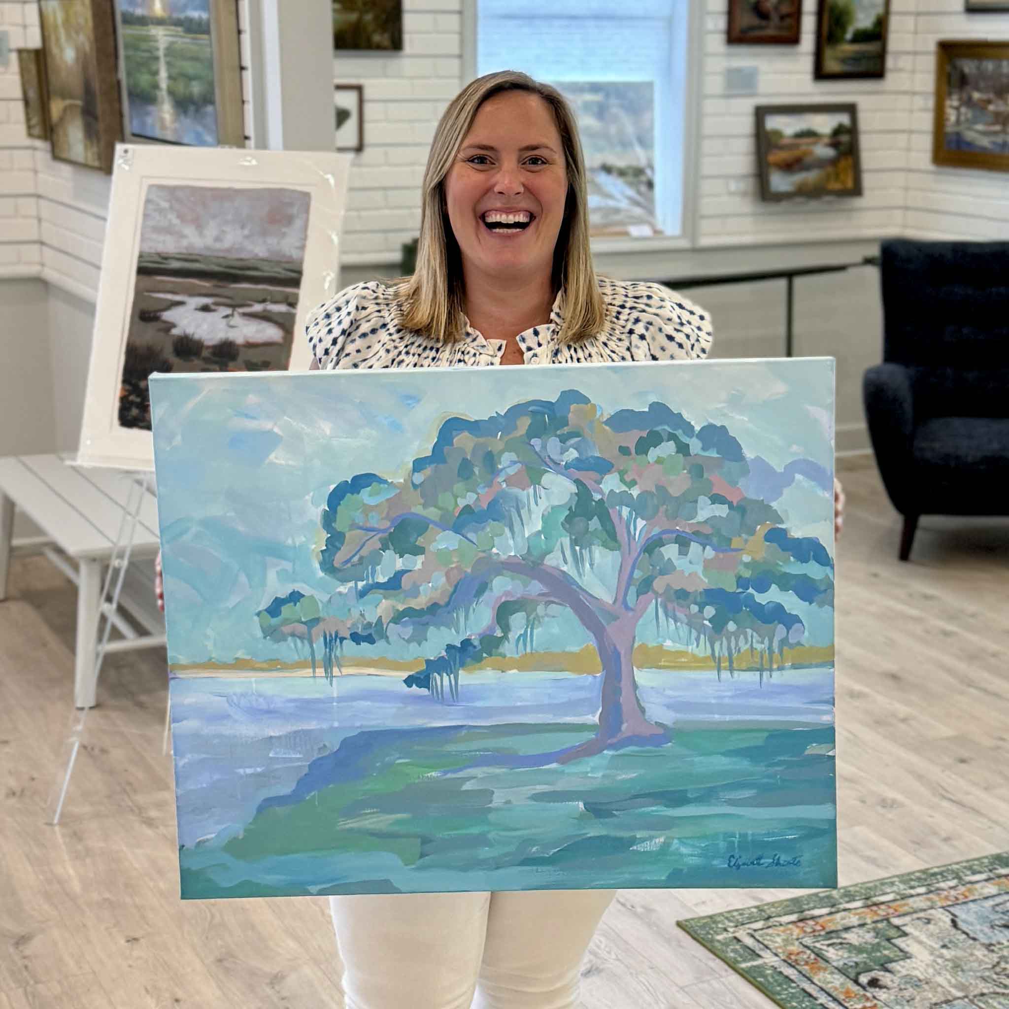 Bordy holding Live Oak Diptych II original acrylic painting by Elizabeth Sheats inside Gray Man Gallery showing scale of the gallery wrapped canvas with a live oak tree and Lowcountry coastal landscape