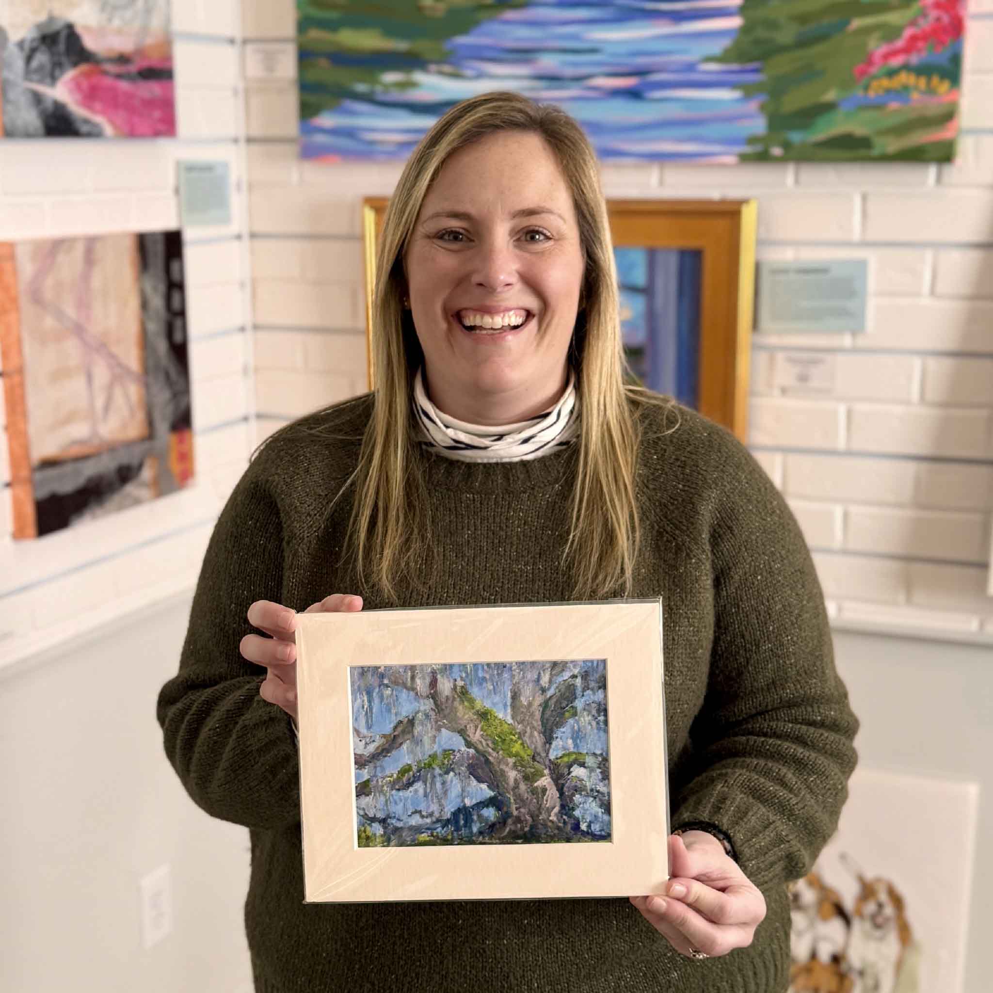 Gray Man Gallery staff member Bordy holding “Enduring Grace” fine art giclée print by Jeanne O’Neal inside the Pawleys Island gallery, featuring a Southern live oak with Spanish moss, professionally matted to standard frame size and ready to display