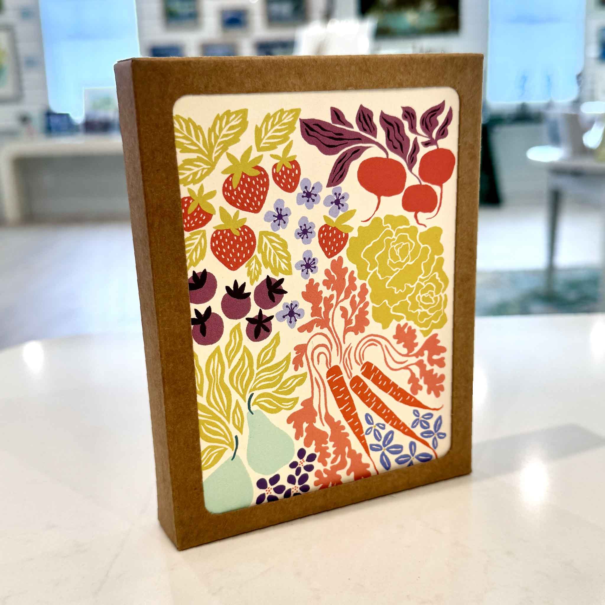 Nuthatch Studio Farmers Market Greeting Card Boxed Set displayed inside Gray Man Gallery in Pawleys Island, South Carolina. This eco-friendly boxed set includes eight assorted greeting cards featuring colorful illustrations of strawberries, pears, carrots, beets, berries, leafy vegetables, and fresh farmers market produce, printed on premium 100% recycled paper with matching recycled kraft envelopes.