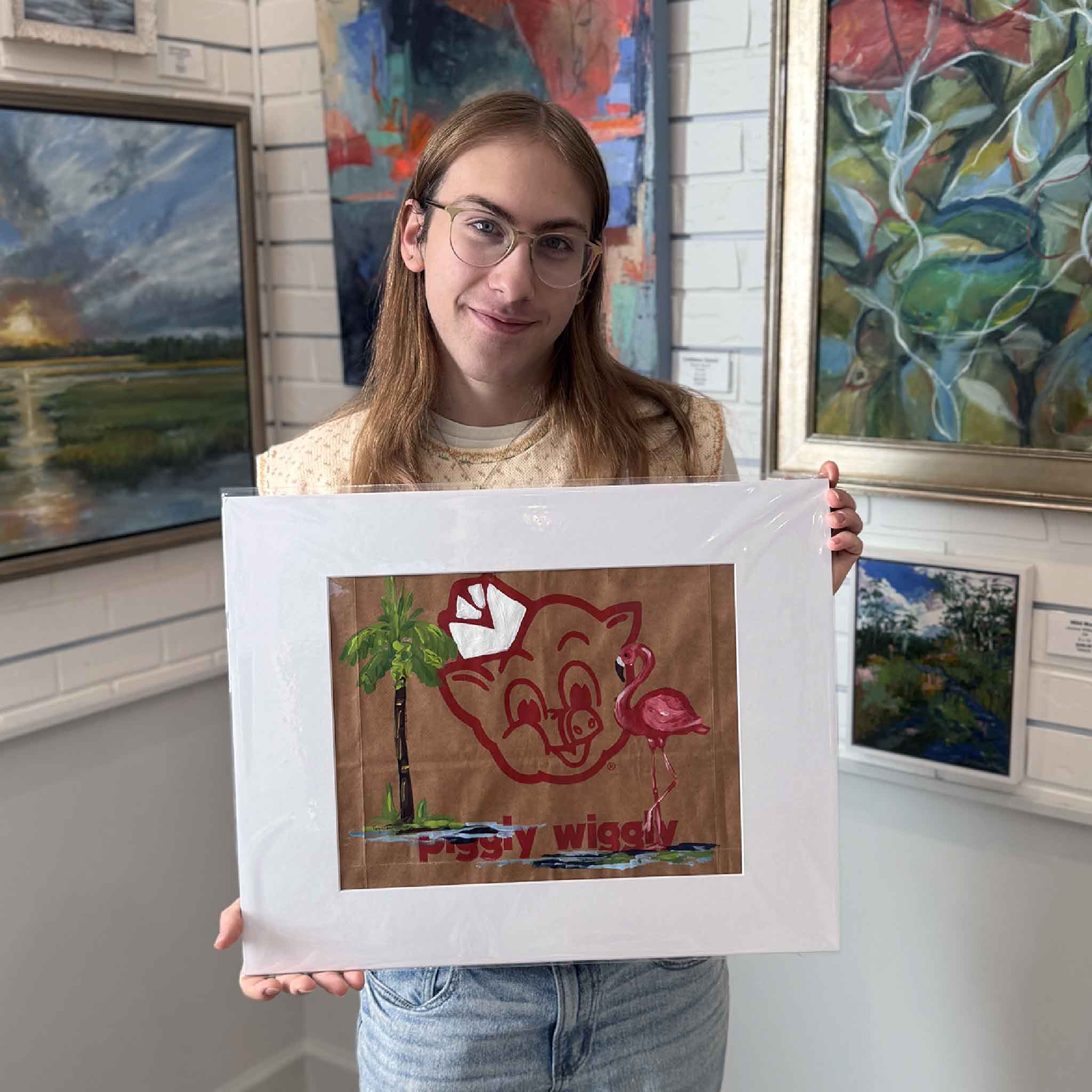 Gallery assistant holding the matted Flamingo & Palm artwork for scale inside Gray Man Gallery.