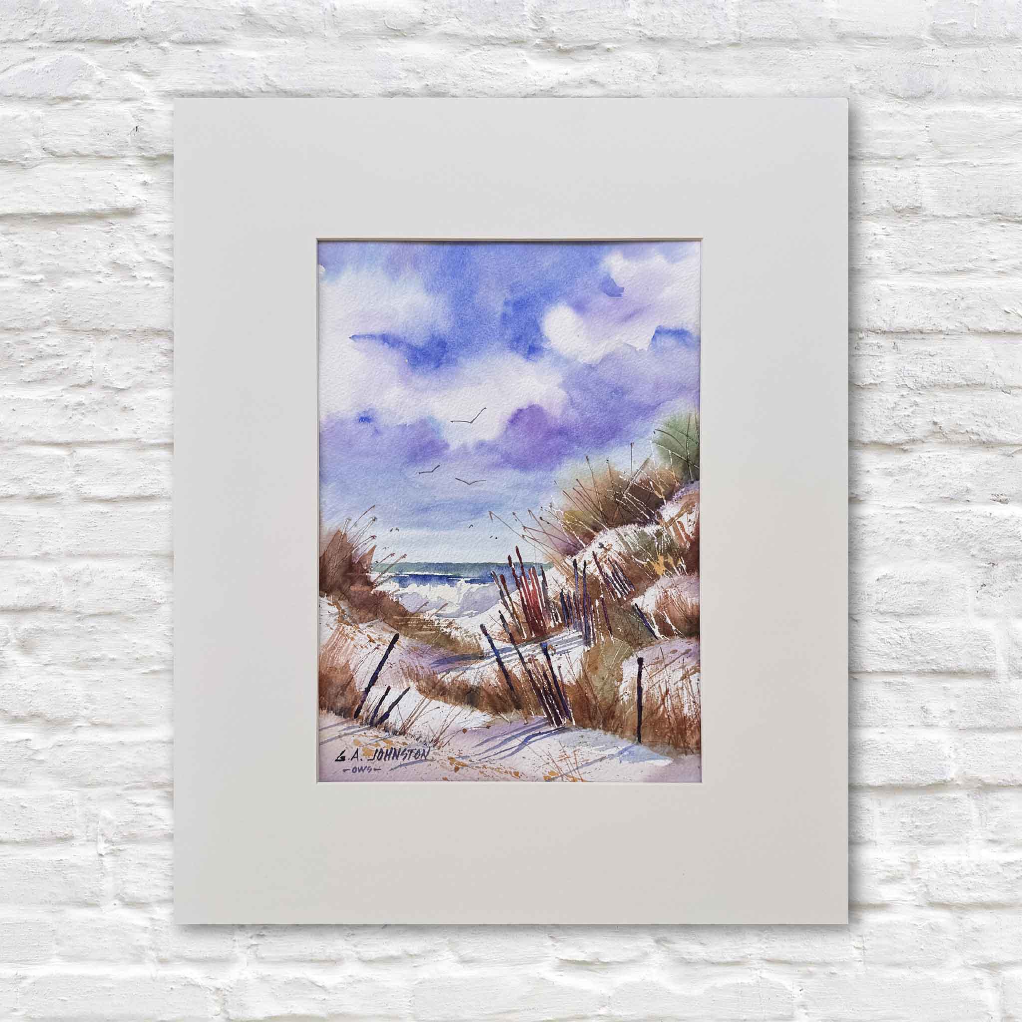 Original watercolor by Gary Johnston titled Dunes at First Light featuring coastal sand dunes with sea grass, weathered fencing, and a glimpse of ocean beyond under a soft blue and violet sky, matted to fit a standard 16x20 frame like those offered at Gray Man Gallery and photographed against a white gallery wall to highlight the vertical composition and Lowcountry coastal atmosphere