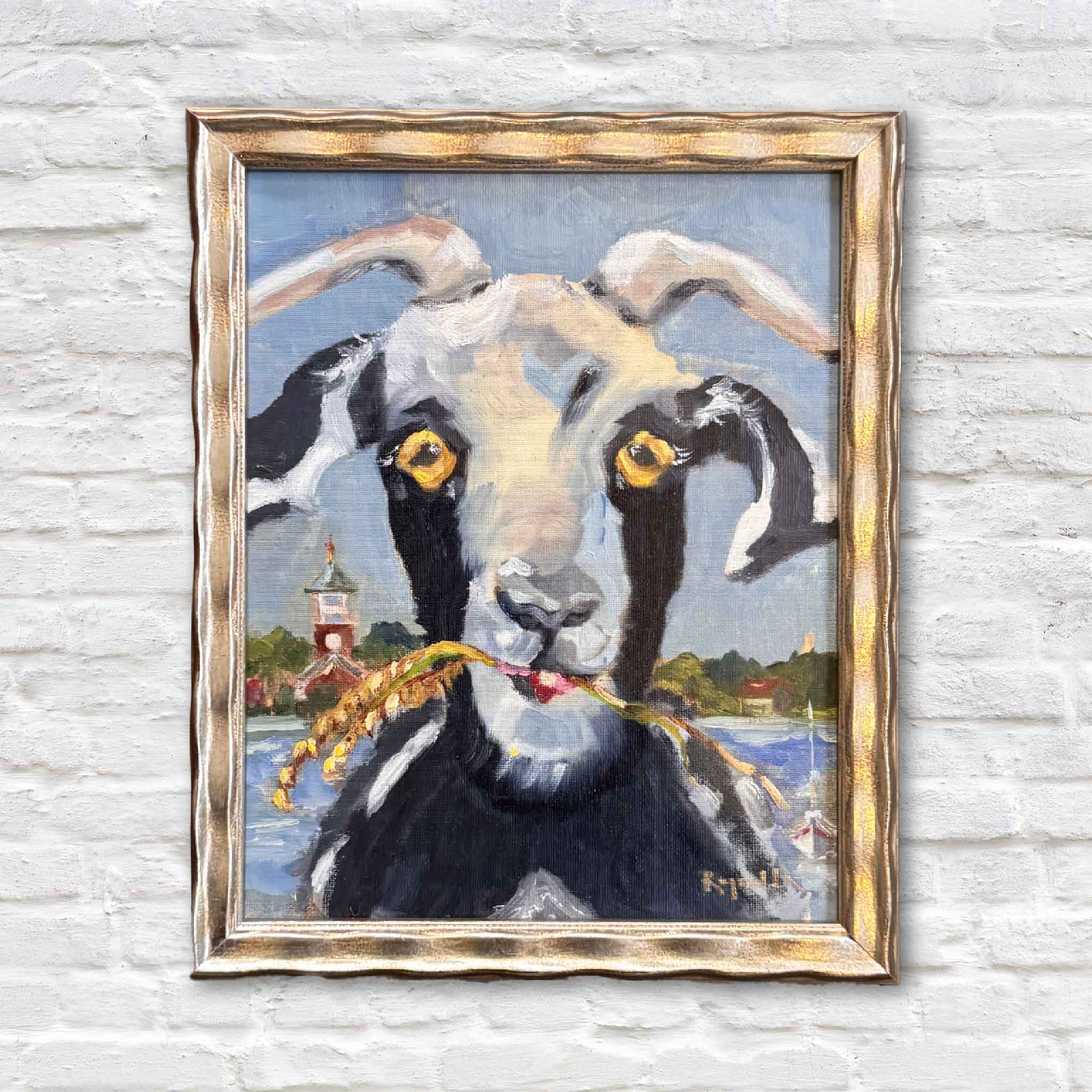 Original oil painting of a goat with golden eyes holding marsh grass in its mouth, Georgetown SC waterfront in the background, framed in champagne.