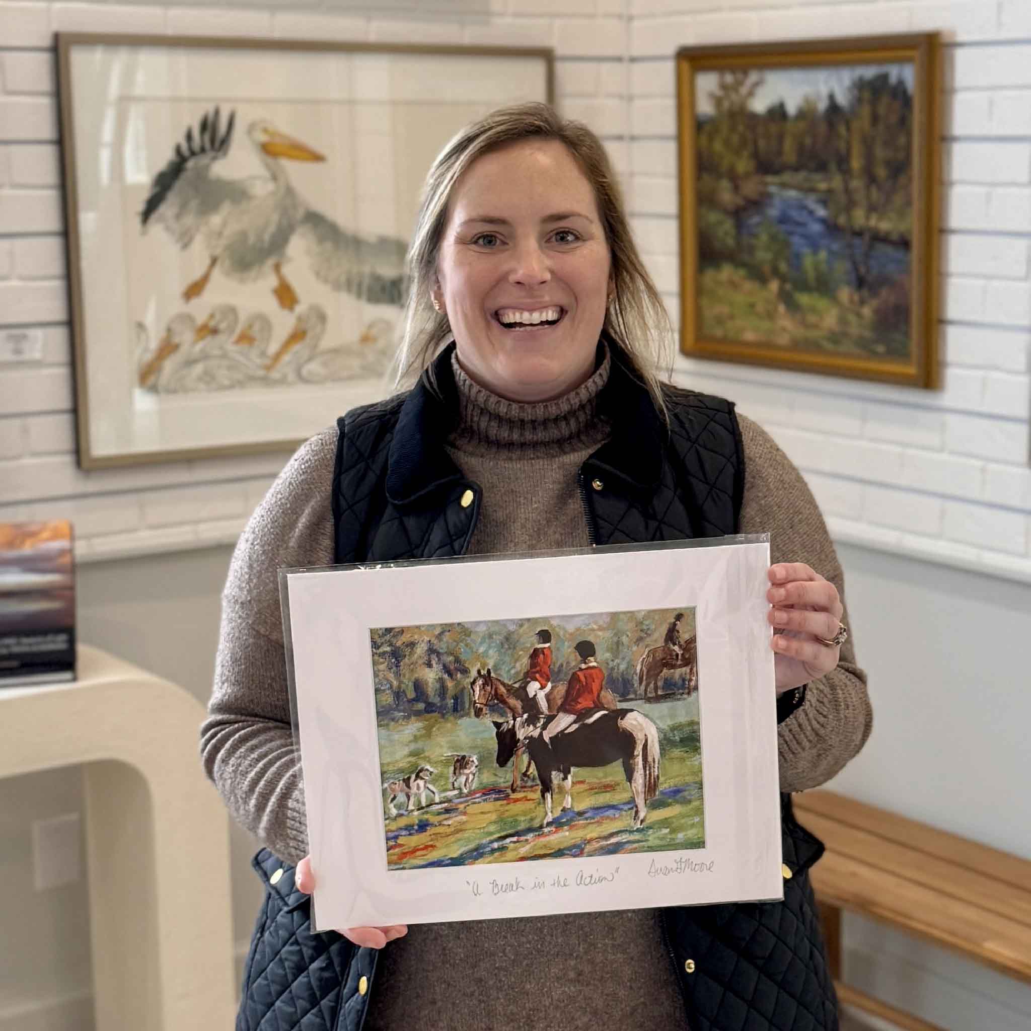 Gray Man Gallery staff member holding signed A Break in the Action print by local artist Susan Moore inside gallery in Pawleys Island SC featuring horseback riders
