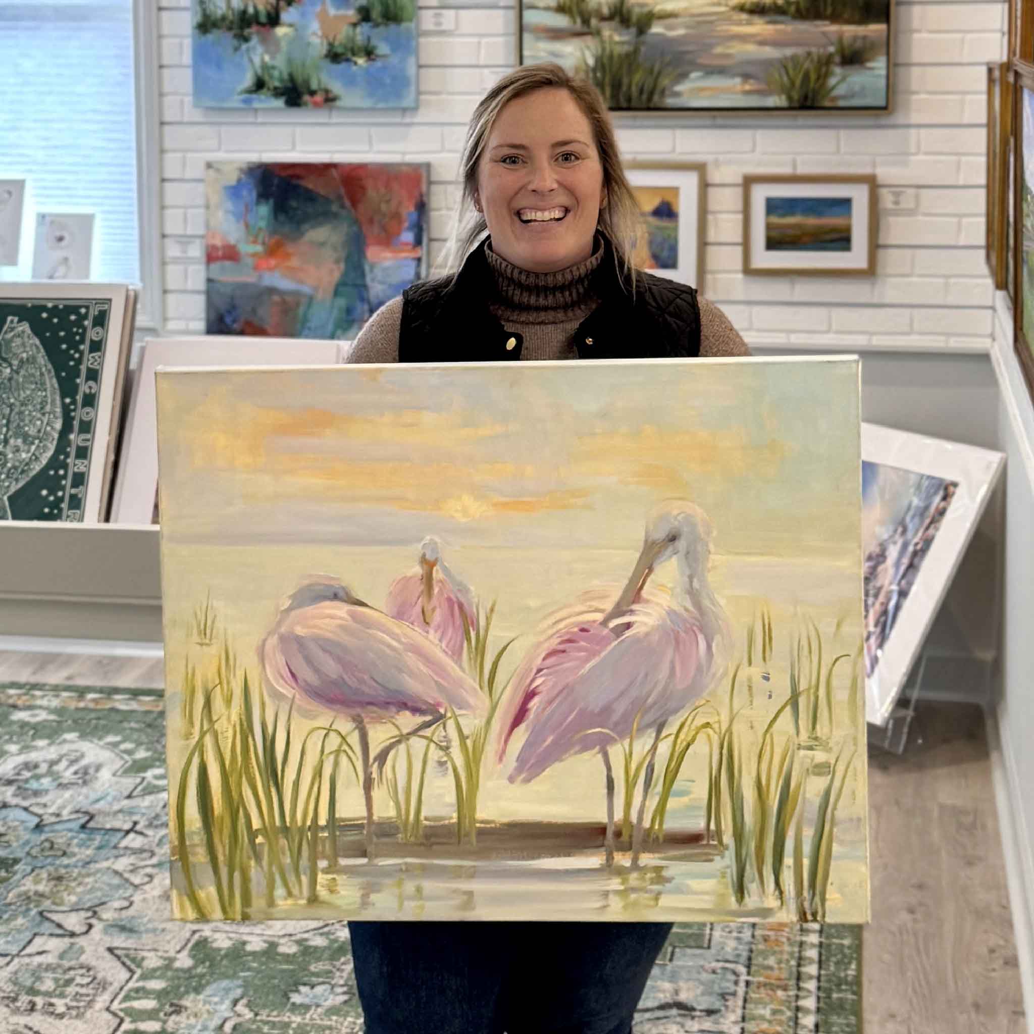 Gray Man Gallery staff member holding Marsh Siesta original oil painting by local artist Helli Luck inside Pawleys Island gallery, showcasing 40x30 Lowcountry marsh artwork with roseate spoonbills