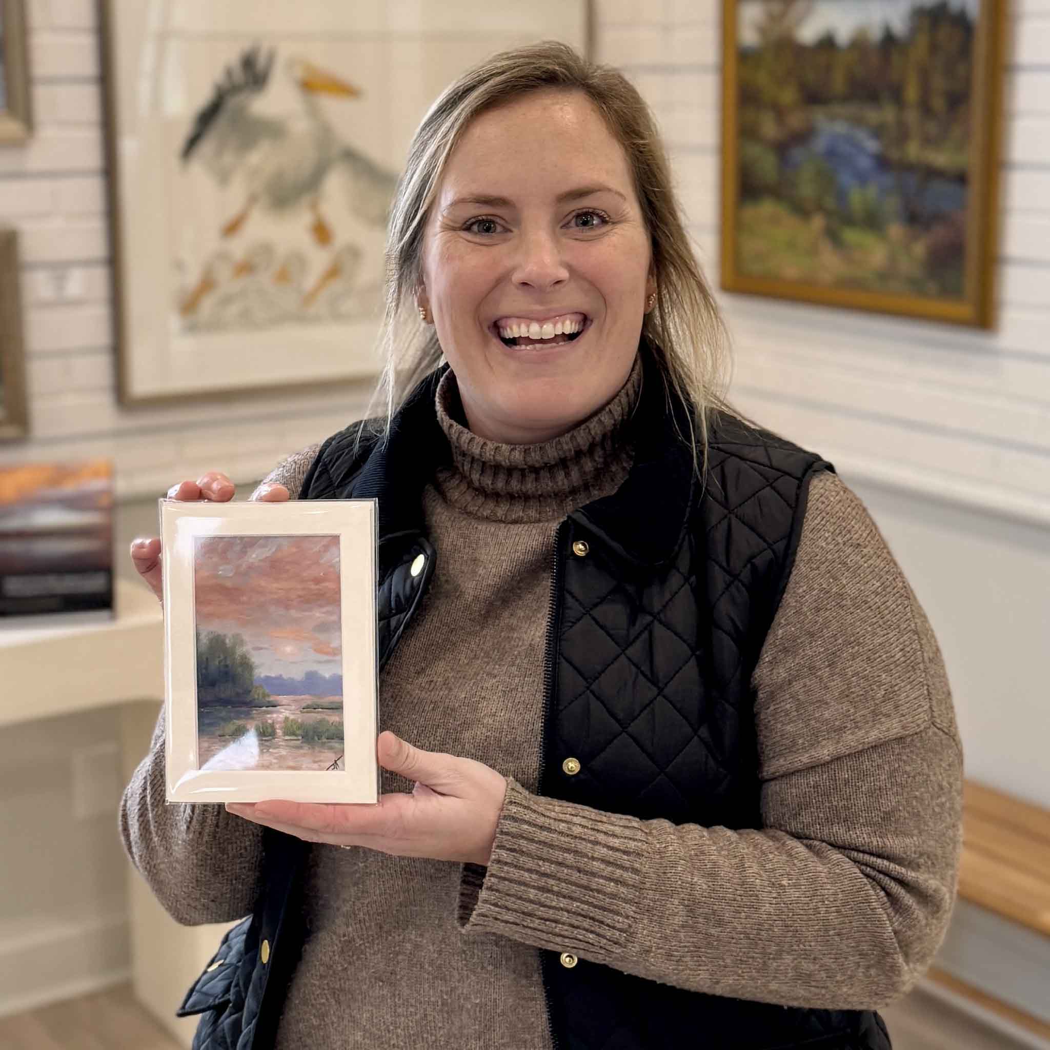 Bordy holding “Quiet After the Storm” fine art print by local Lowcountry artist Jamie Arnold inside Gray Man Gallery in Pawleys Island, South Carolina, showcasing coastal marsh sunset artwork and custom framing