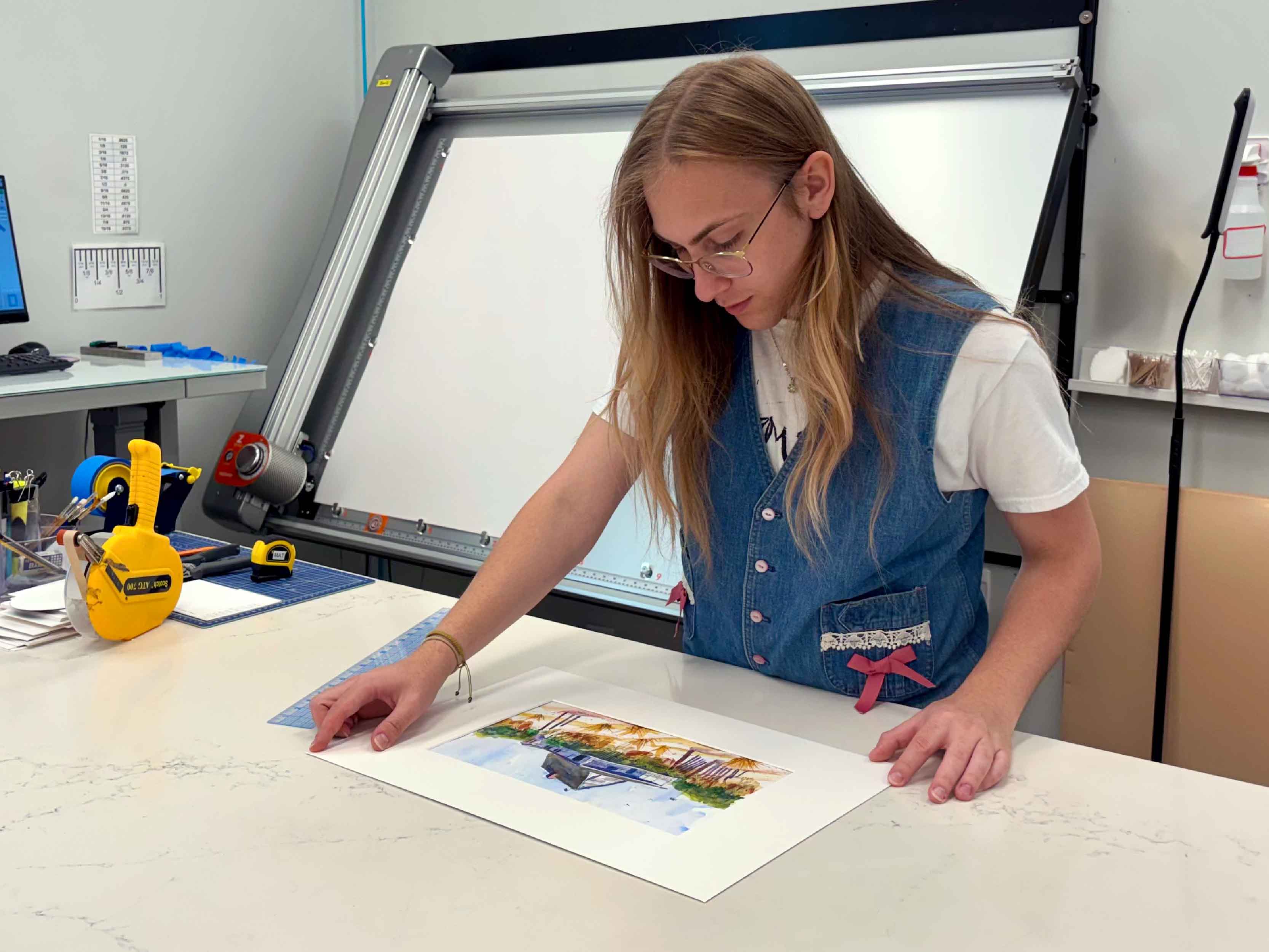 Custom framing specialist Alex measures original watercolor artwork at Gray Man Gallery in Pawleys Island, South Carolina, carefully checking alignment, spacing, and mat placement to create a conservation-quality custom picture frame with professional precision and lasting protection.