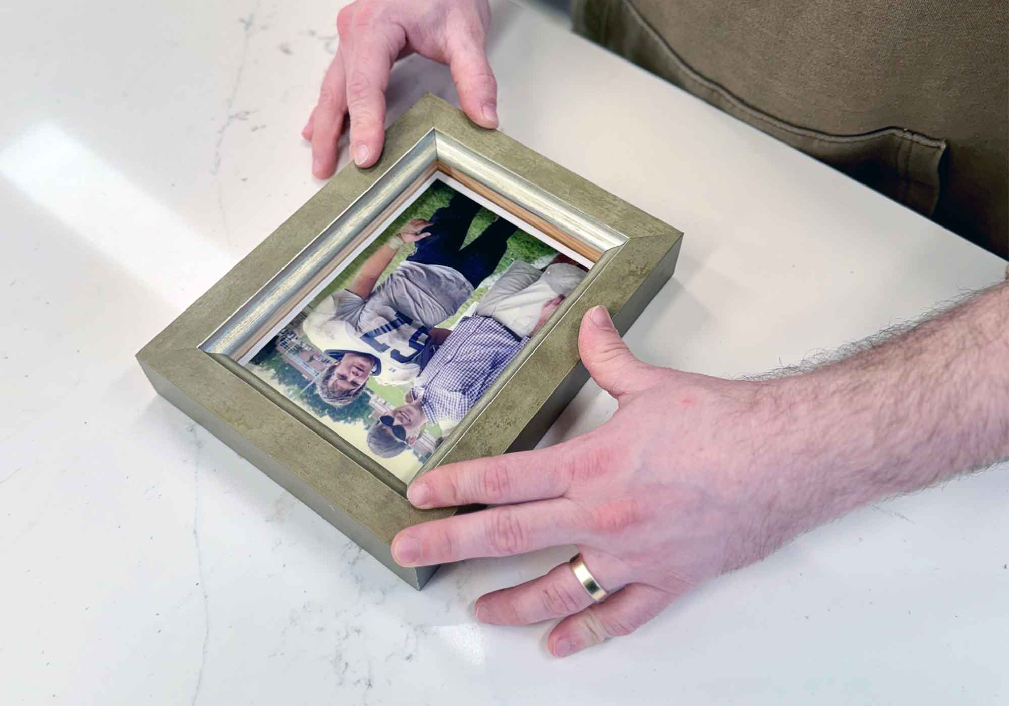 Peyton hand-finishing a custom framing project at Gray Man Gallery in Pawleys Island, South Carolina, carefully fitting a photograph into a handcrafted frame using museum-quality materials, preservation techniques, and local artisan craftsmanship for fine art, photography, and meaningful family keepsakes.