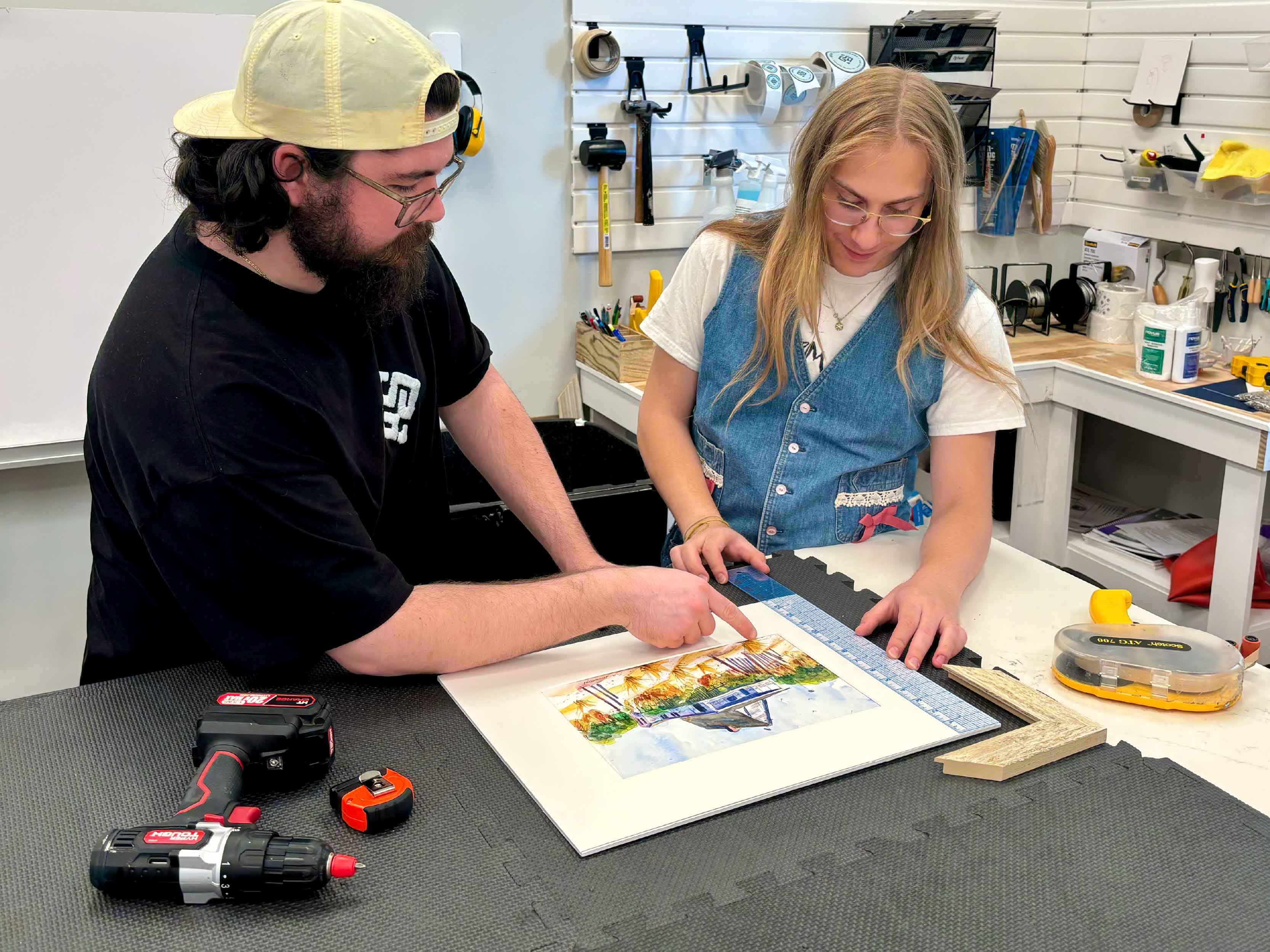 Gray Man Gallery custom framers Peyton and Alex work together to align original watercolor artwork, evaluate mat spacing, and prepare conservation-quality materials during the custom picture framing process in Pawleys Island, South Carolina, creating a beautifully balanced presentation designed to protect the artwork for years to come.