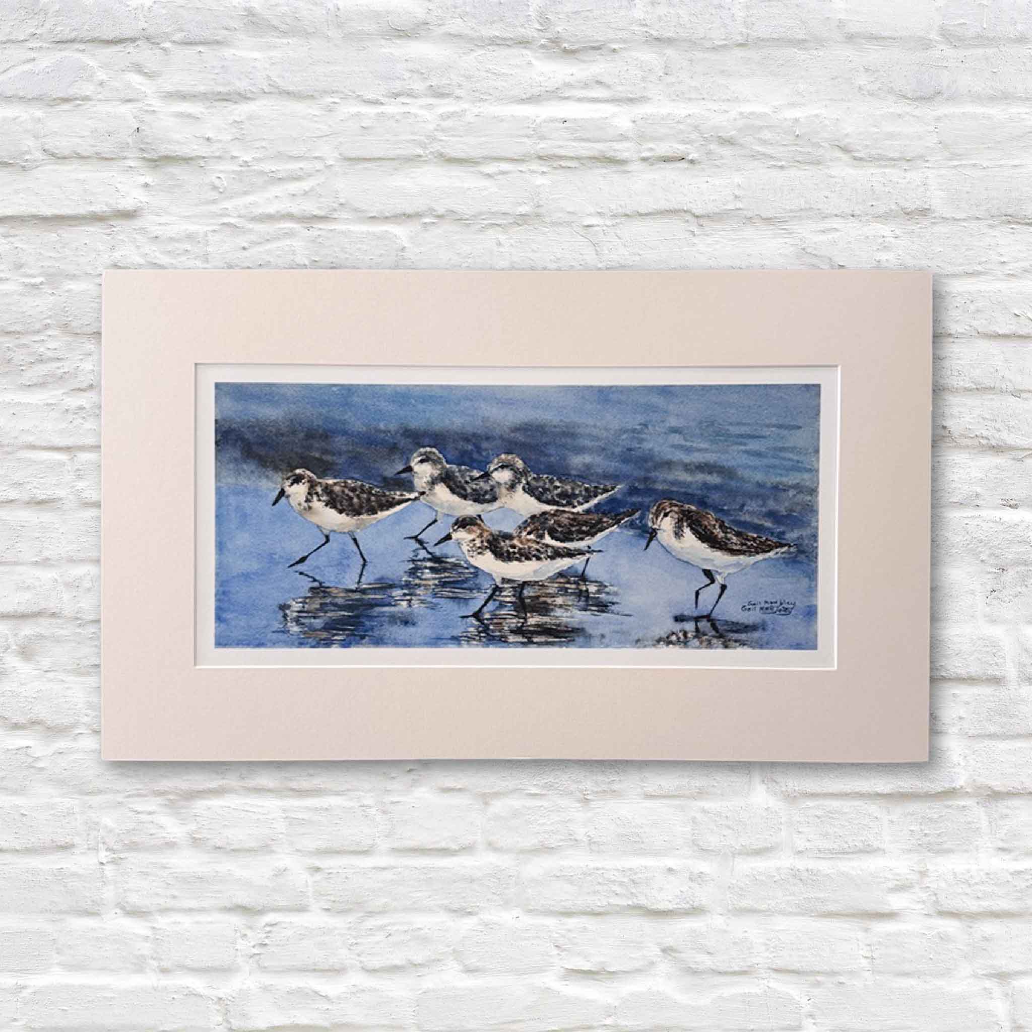 Sanderlings watercolor print by Gail Joley showing a small flock of shorebirds walking along wet sand, reflected in shallow coastal water, photographed at Gray Man Gallery in Pawleys Island.