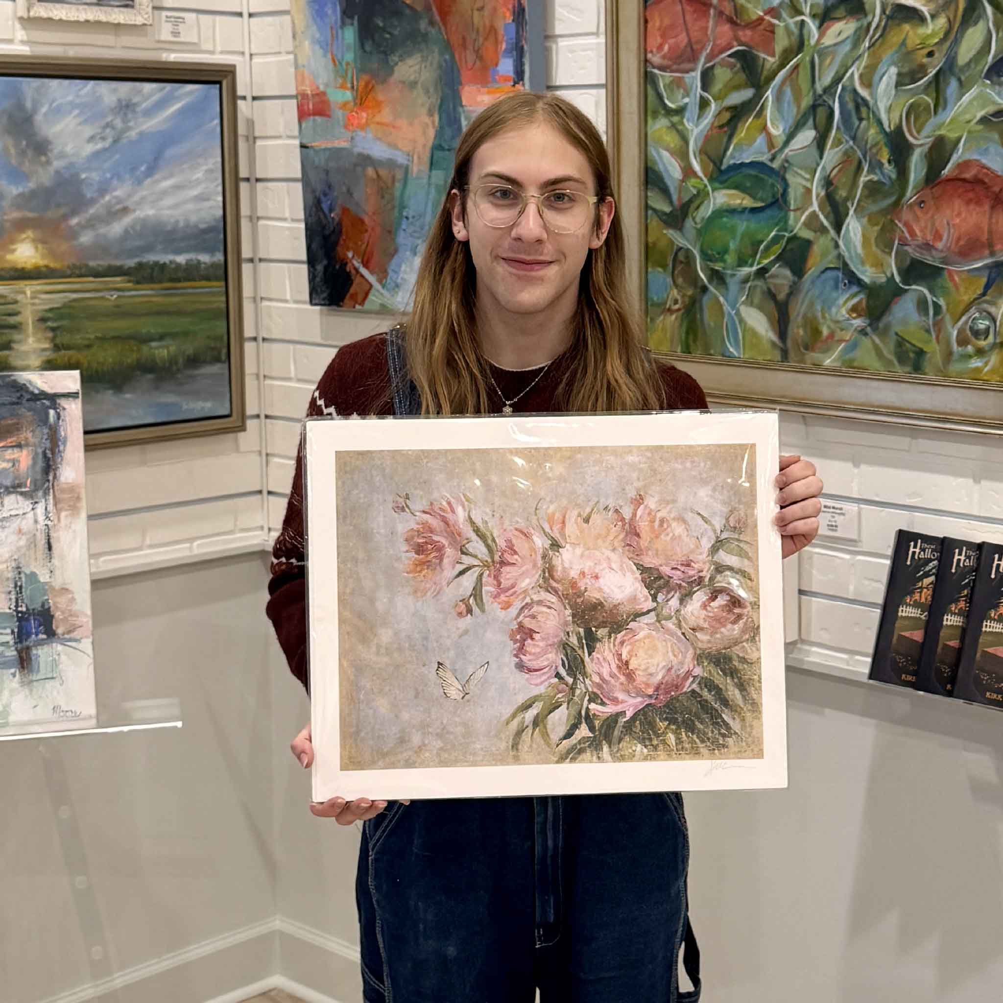 Gray Man Gallery team member holding helli luck floral peonies art print inside gray man gallery with colorful paintings displayed behind