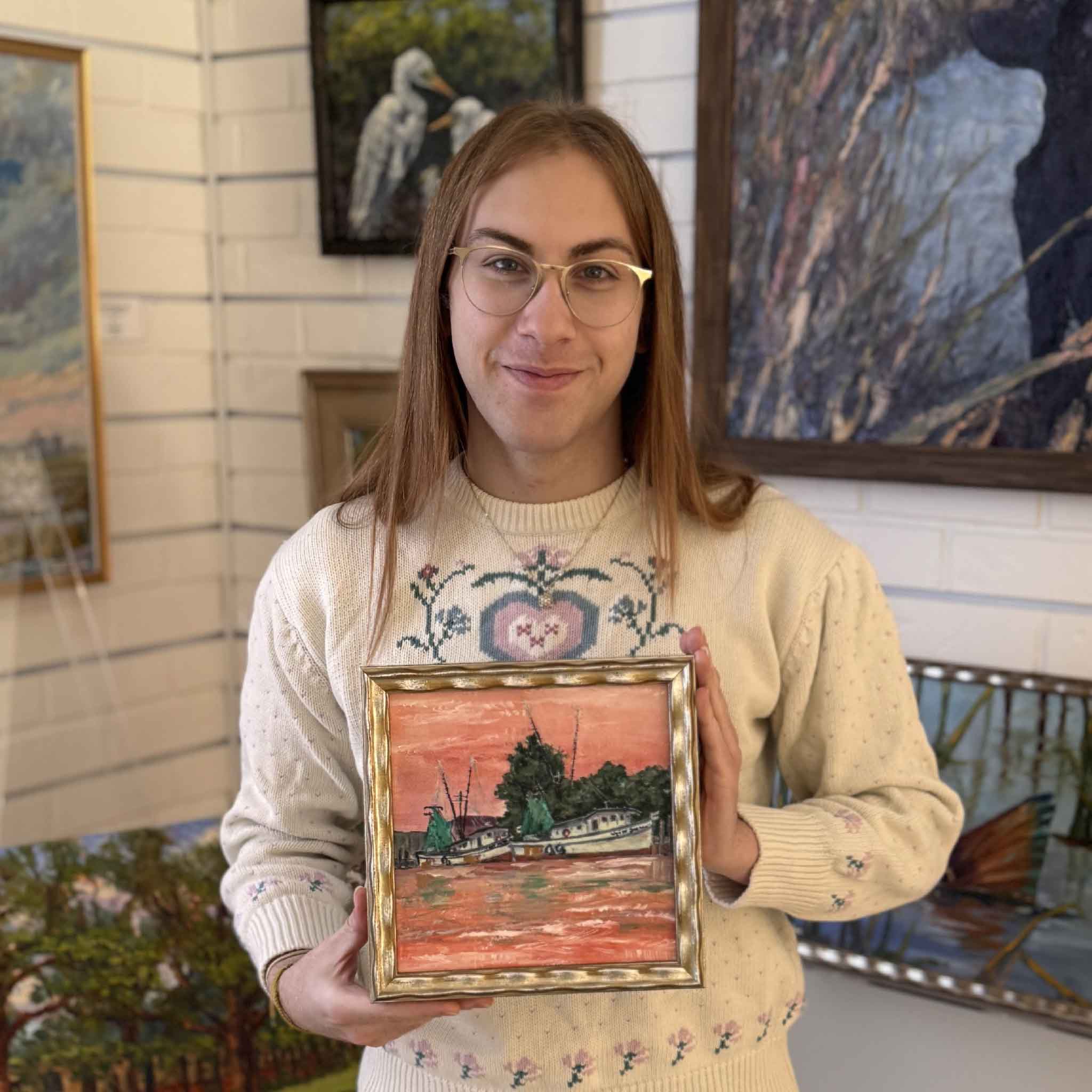 Gray Man Gallery team member holding framed fine art giclée of Harbor Reflections by Jeanne O’Neal, showing shrimp boats resting along the Georgetown harbor beneath a coral sky.