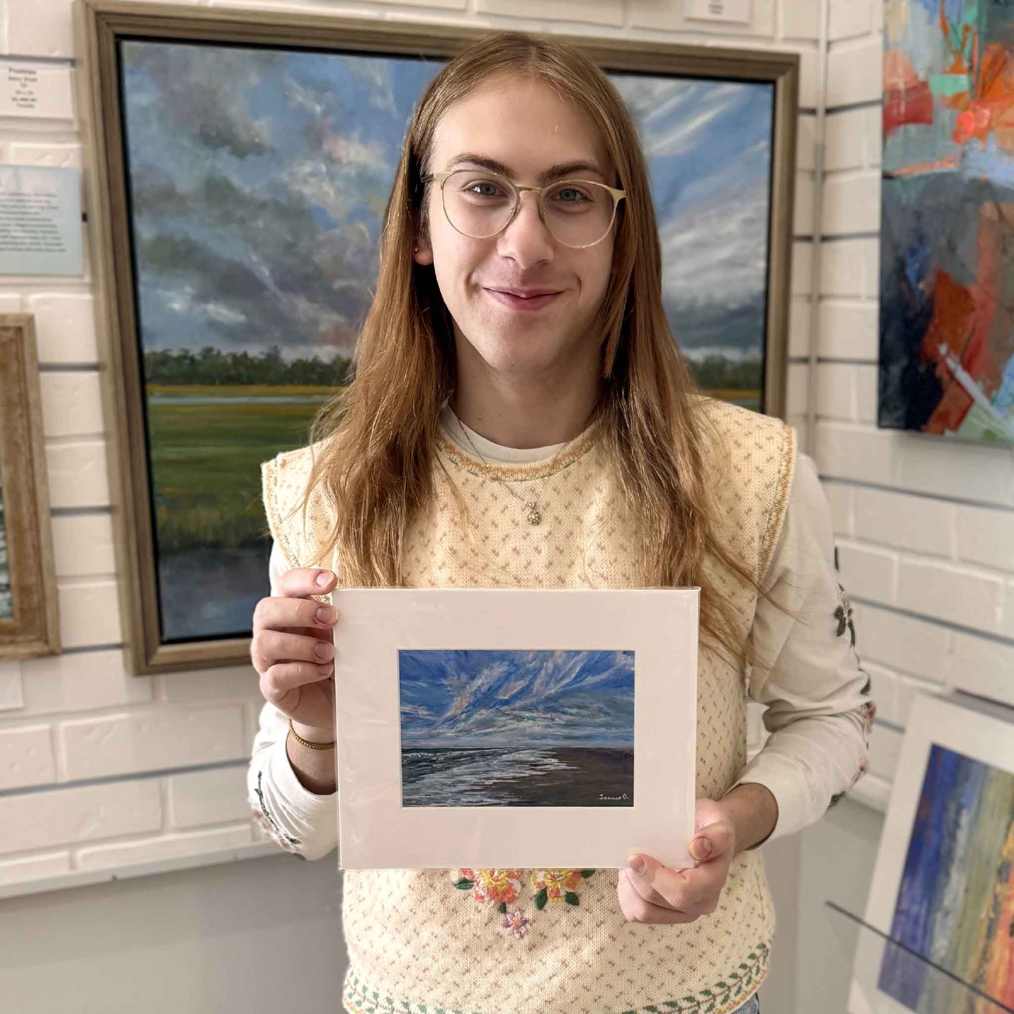 A Gray Man Gallery team member holds Looking South, an 8×10 matted giclée by Jeanne O’Neal, shown for scale inside the gallery.