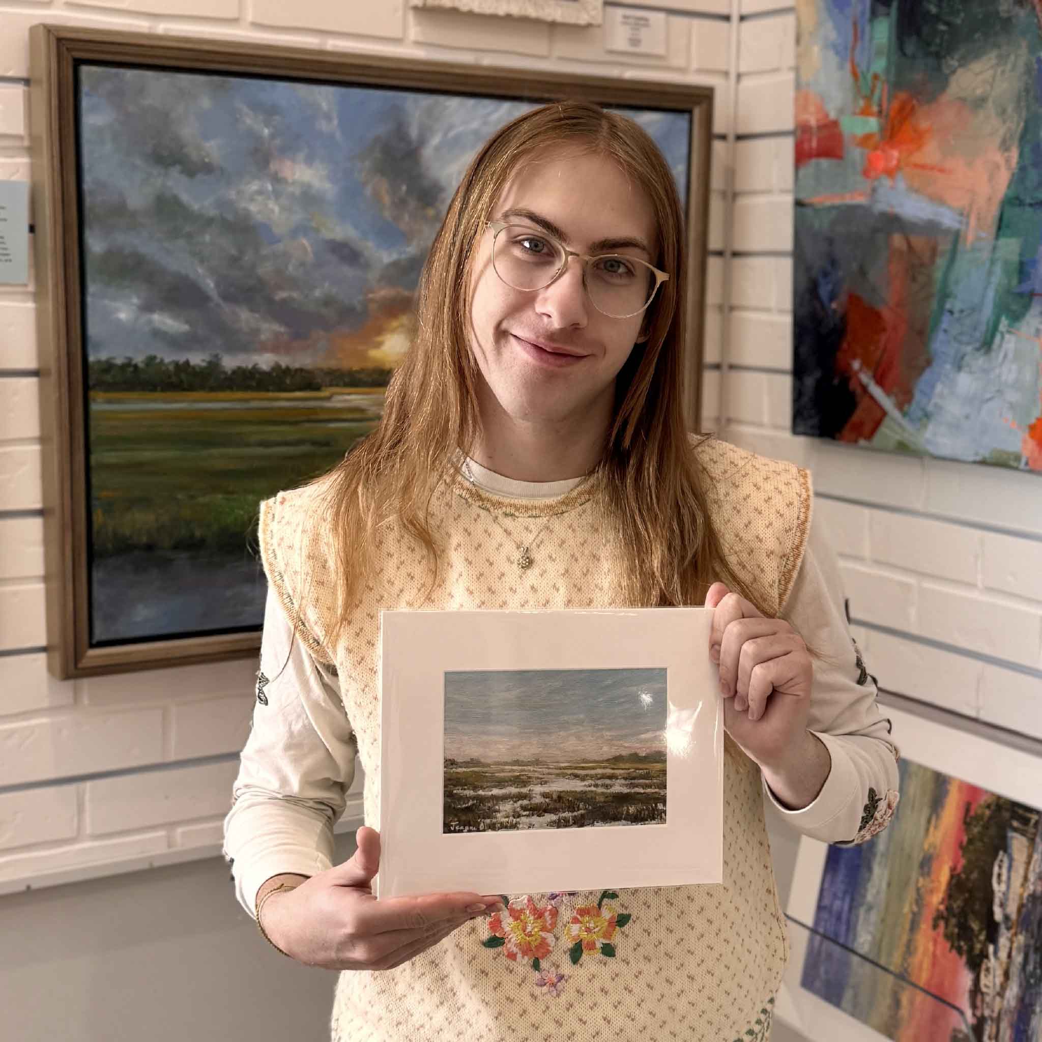 A Gray Man Gallery team member holds Soft Breeze, an 8×10 matted giclée by Jeanne O’Neal, shown for scale inside the gallery.