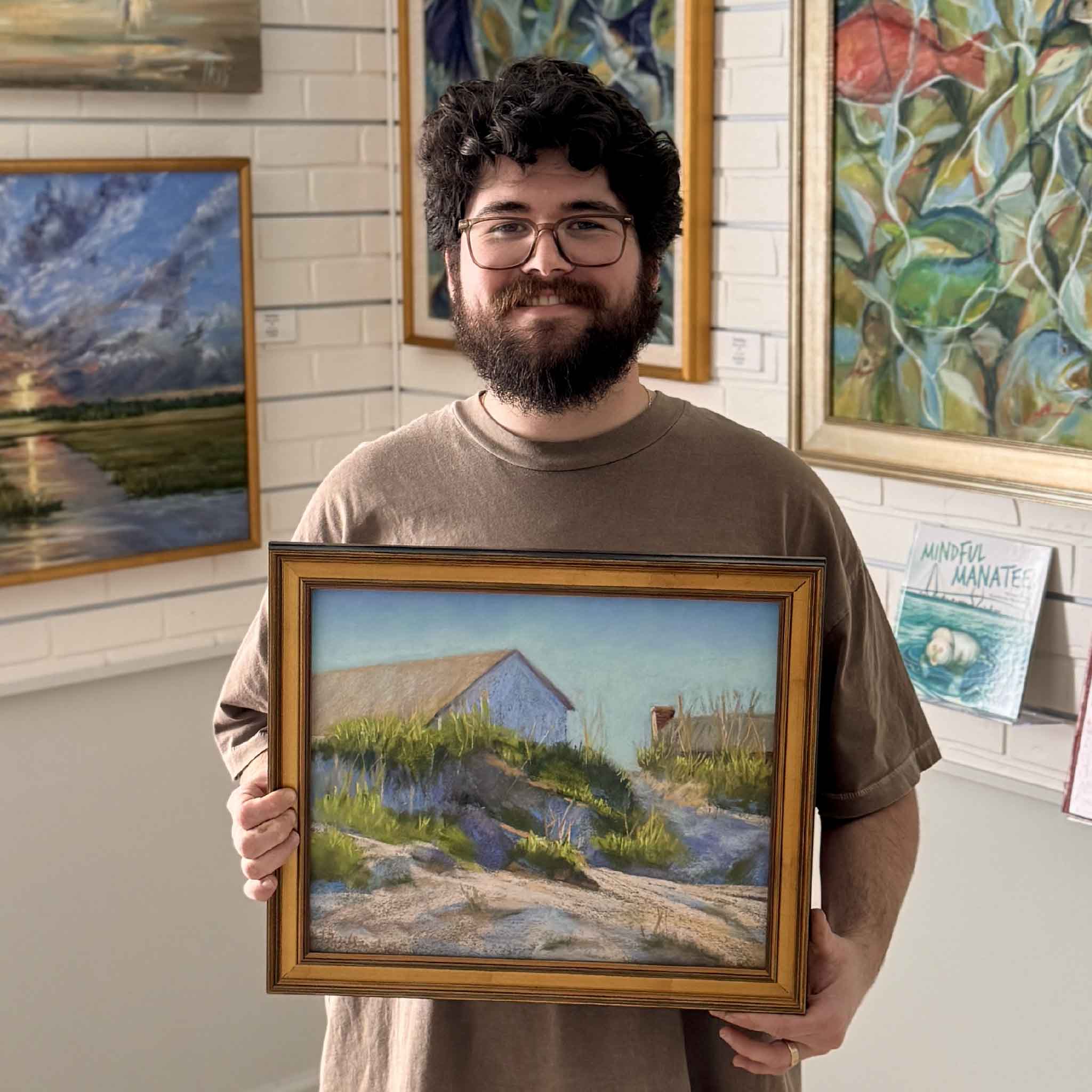 Original pastel Neighbors by Joanne Willoughby shown held for scale inside Gray Man Gallery, illustrating the artwork’s size, framing, and warm coastal palette in a real gallery setting.