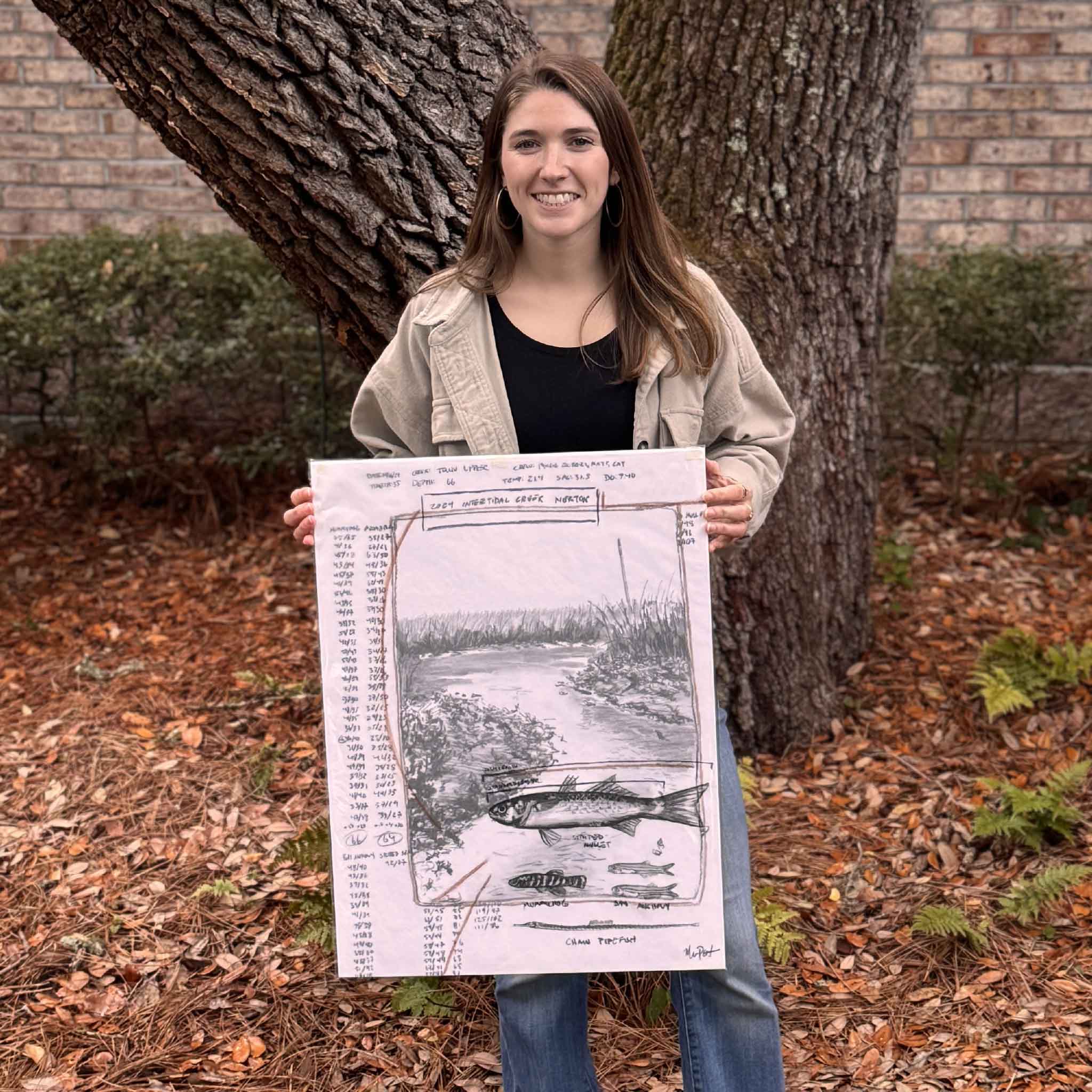 Local artist Maggie Pelton holds her 18 x 24 original charcoal work Intertidal Creek Nekton outdoors, shown for scale and photographed at Gray Man Gallery.