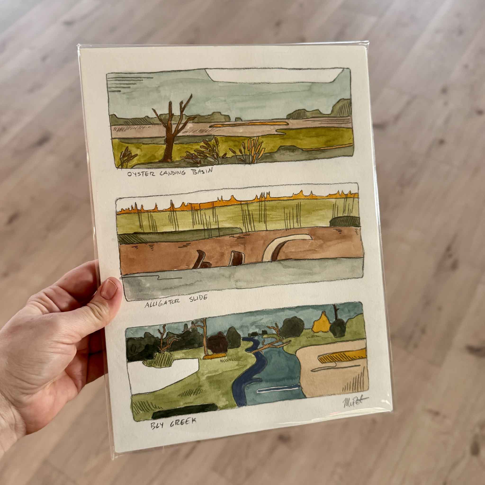 Handheld view of North Inlet Marsh Triptych, an original watercolor by Maggie Pelton, showing three miniature marsh landscapes inspired by the tidal waterways of Georgetown, South Carolina.