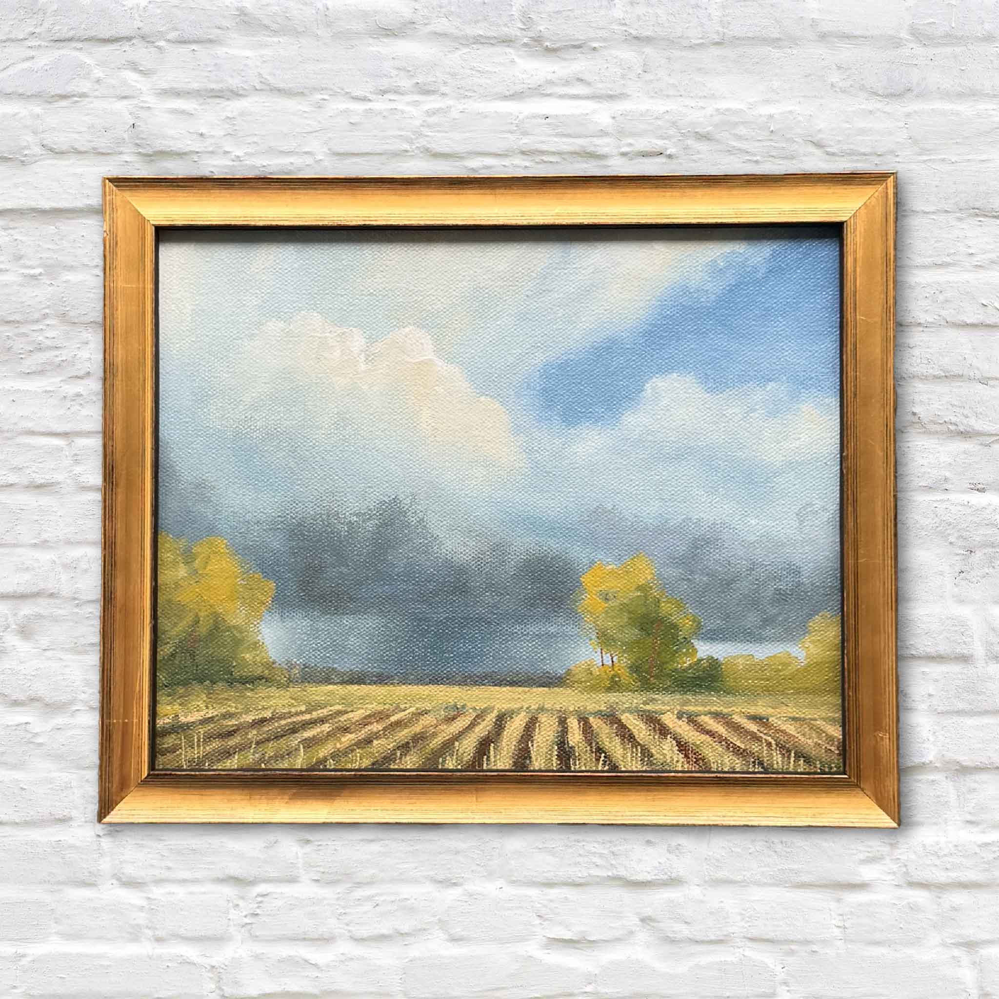Mayfields original oil painting by Lowcountry artist Jamie Arnold, framed in a classic gold frame and displayed at Gray Man Gallery in Pawleys Island, South Carolina, featuring a dramatic sky rolling over plowed fields in a Southern coastal landscape