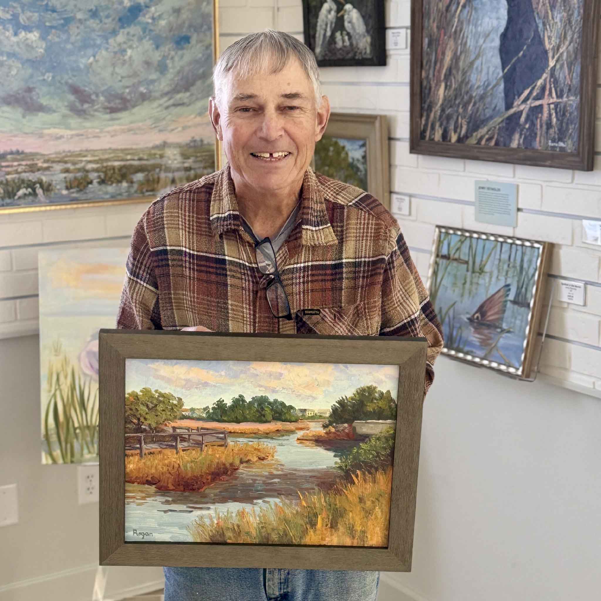 Local Pawleys Island artist Michael Rogan holding his original oil painting of the South Litchfield Causeway marsh at Gray Man Gallery