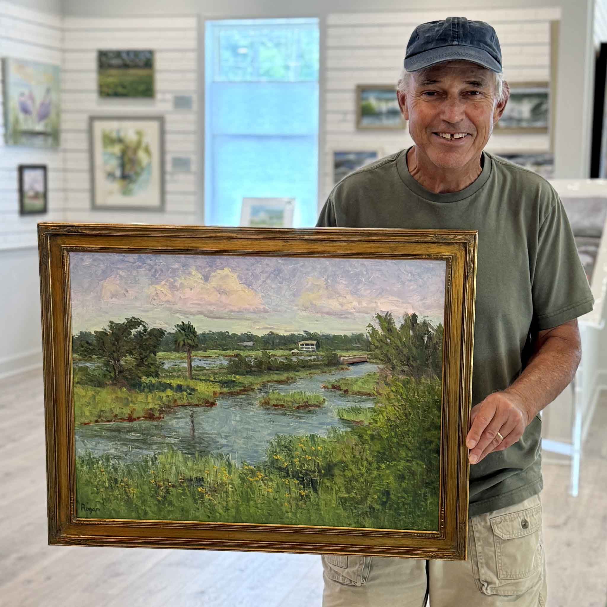 Artist Michael Rogan holding Summer in Litchfield, an original oil painting depicting one of South Litchfield's best-known marsh and tidal creek views. Framed original artwork available at Gray Man Gallery in Pawleys Island, South Carolina.