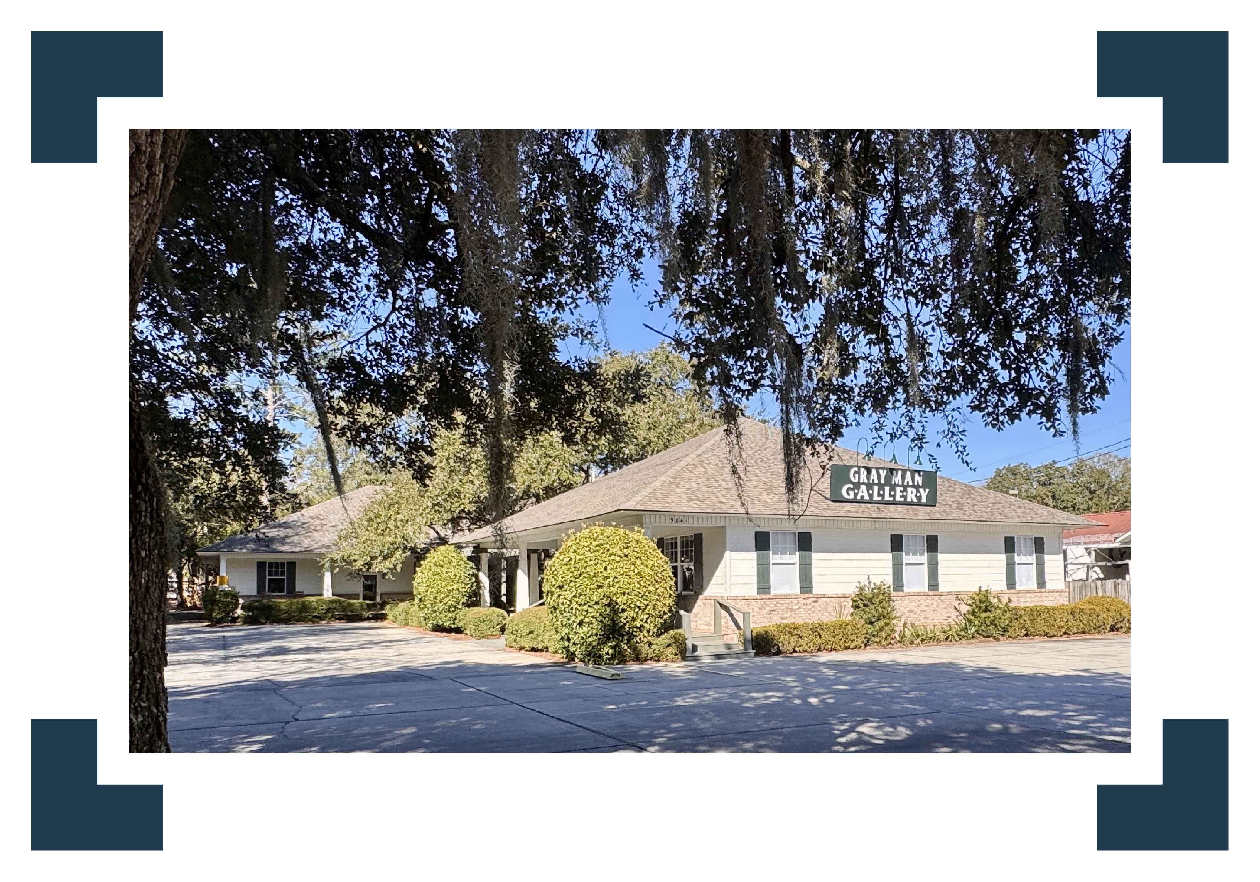 Exterior view of Gray Man Gallery in Pawleys Island, South Carolina, situated along Ocean Highway beneath mature live oak trees and Spanish moss. This established Lowcountry art gallery showcases original artwork by local and regional artists and offers custom framing services, serving collectors throughout Georgetown County and the South Carolina coast.