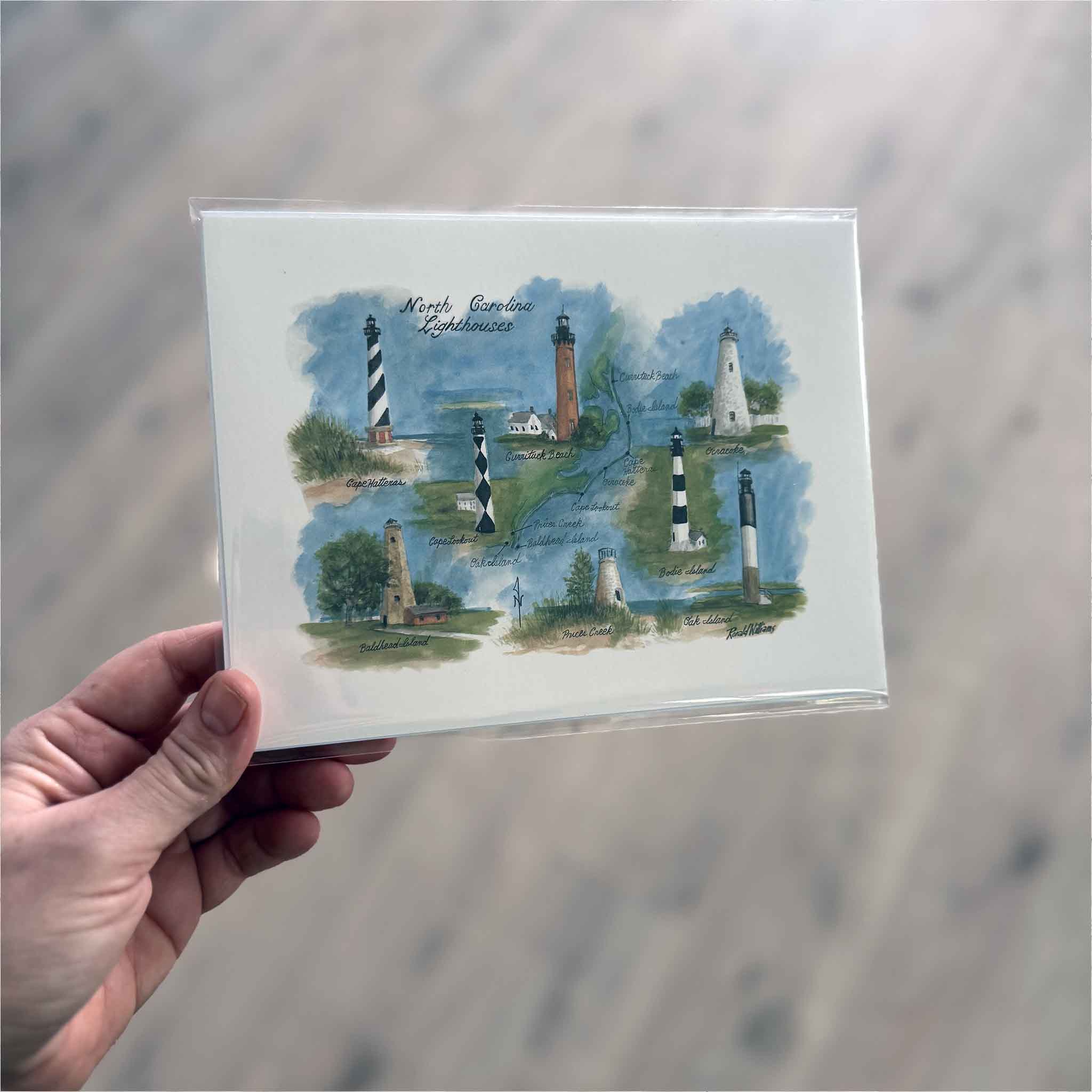 Hand holding N.C. Lighthouses by Ronald Williams, an 8 x 6 inch watercolor map print highlighting North Carolina lighthouses, shown for size and detail at Gray Man Gallery in Pawleys Island, SC.