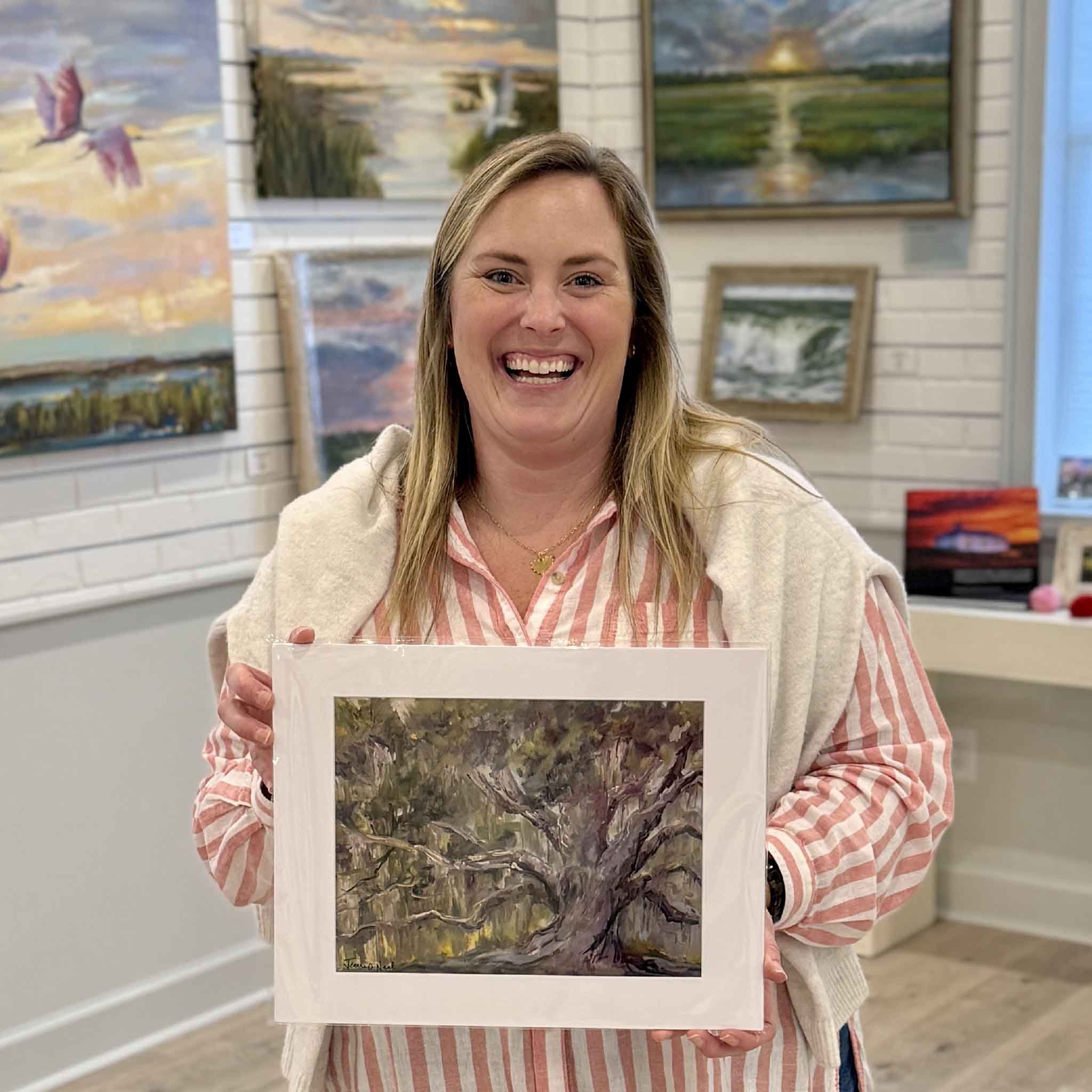 Bordy holding Tell Me a Story fine art giclée print by Jeanne O’Neal inside Gray Man Gallery in Pawleys Island, South Carolina, featuring a Southern live oak from the Among the Trees collection