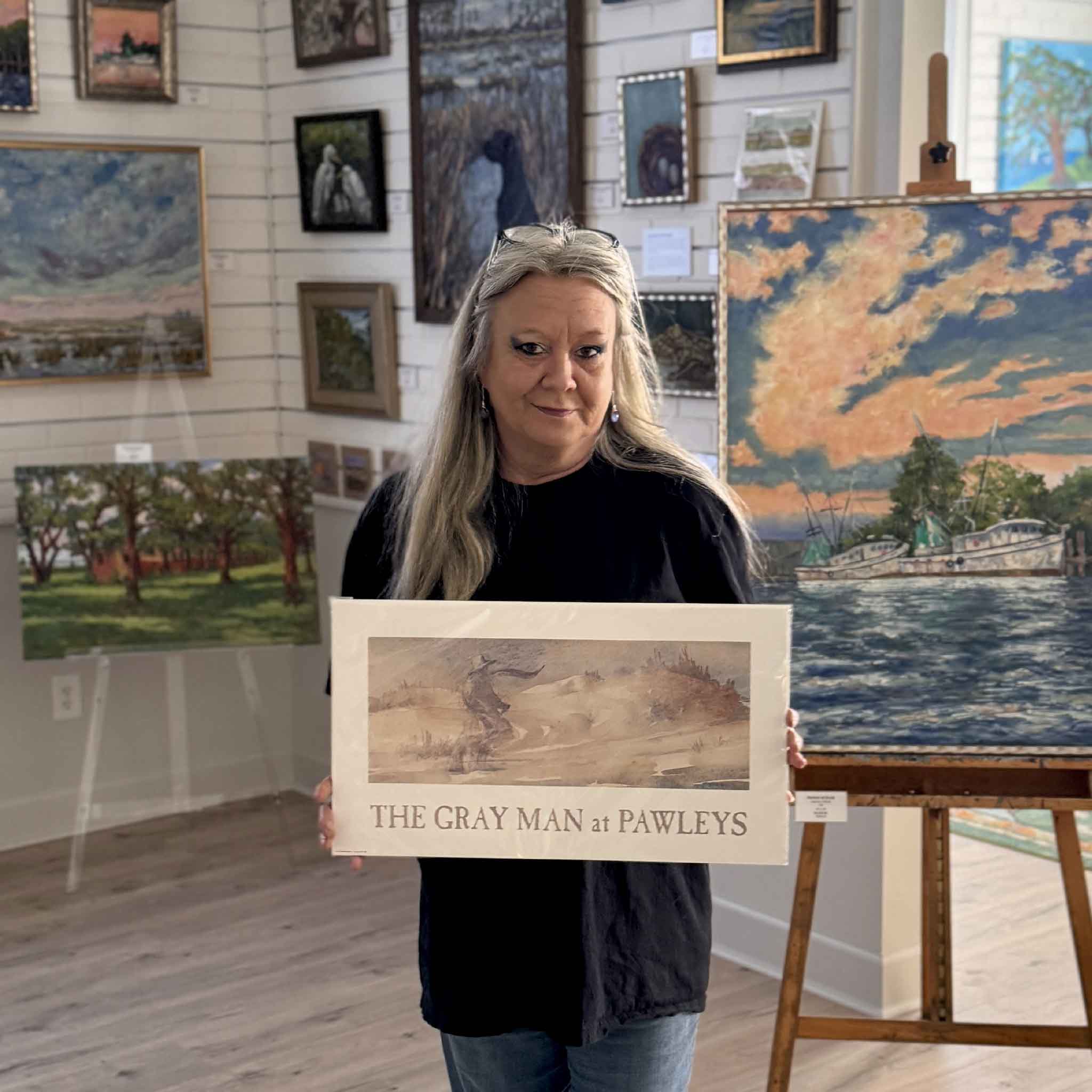 Artist Eleanor Spruill holding The Gray Man at Pawleys watercolor print inside Gray Man Gallery, the only place in the world this iconic Pawleys Island artwork is available.