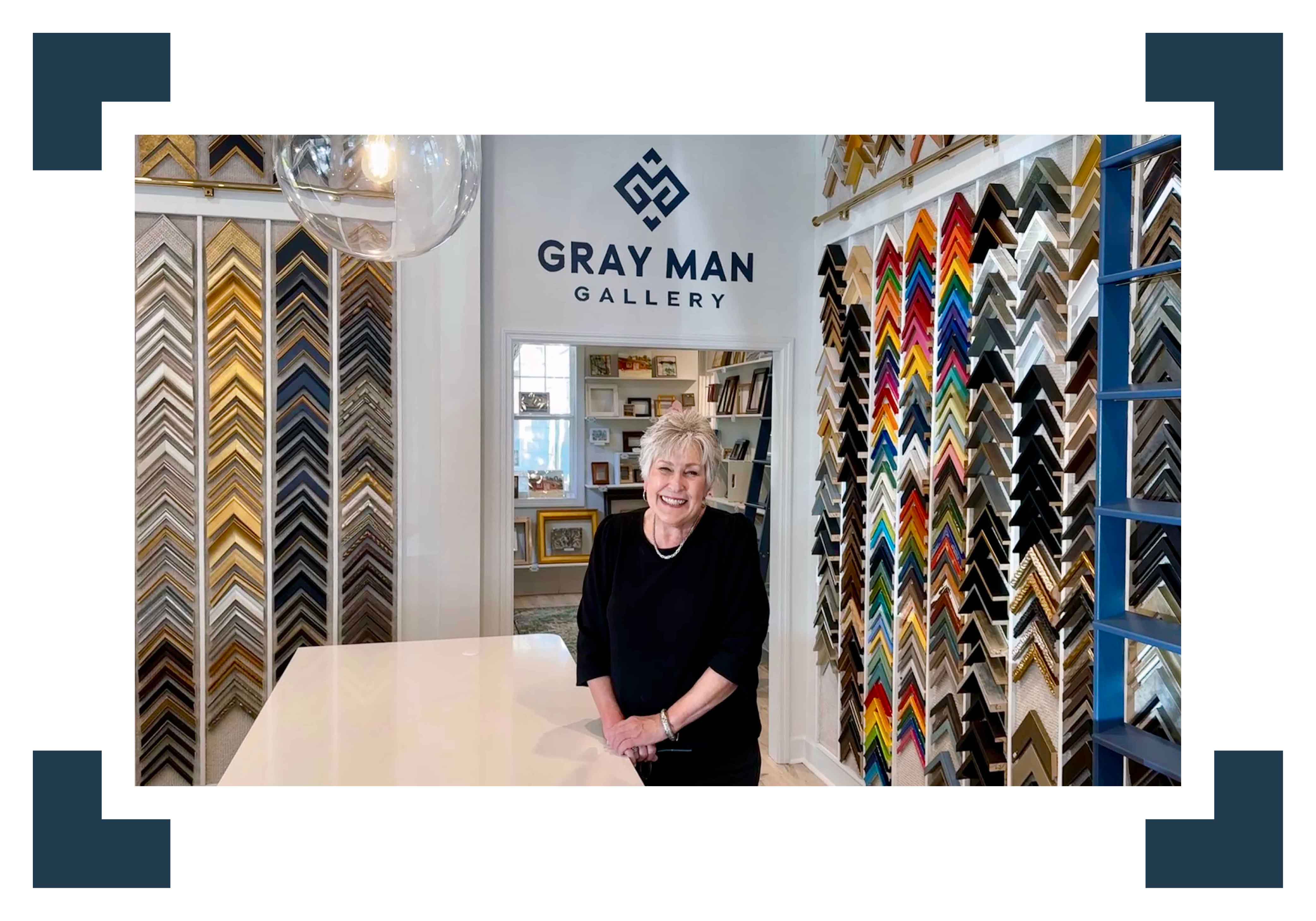 Vida Miller, founder of Gray Man Gallery in Pawleys Island, standing in the custom framing design studio surrounded by frame samples, showcasing fine local art and professional framing services since 1980