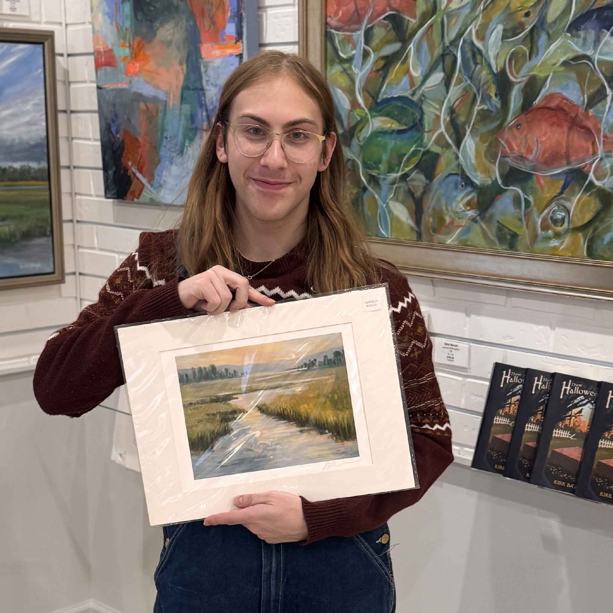 Customer holding the matted “Coming Home” giclée print by Helli Luck inside Gray Man Gallery with surrounding coastal artwork.