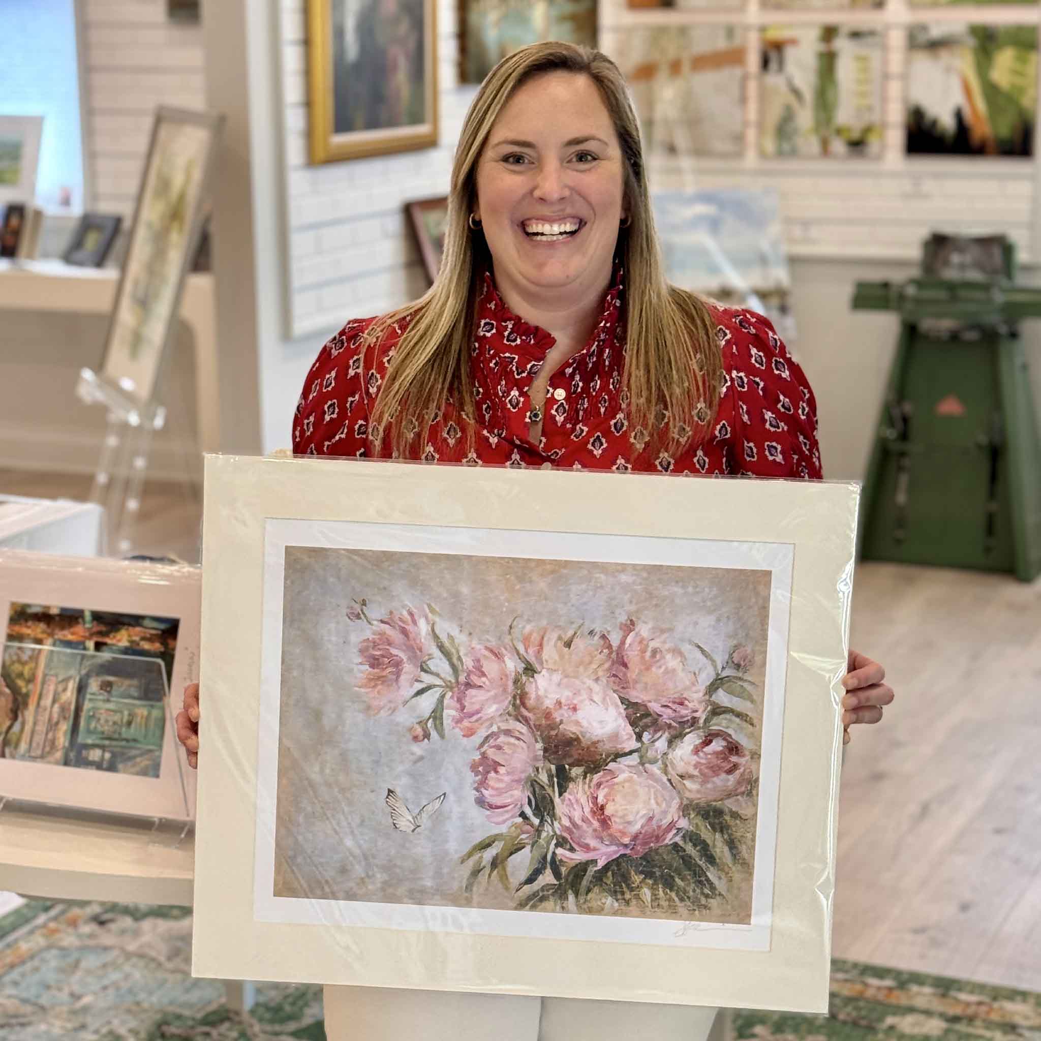 Gray Man Gallery staff member Bordy holding From Her Garden floral giclée print by artist Helli Luck to show scale, featuring romantic pink peonies and butterfly detail, professionally matted to standard 20x24 frame size.