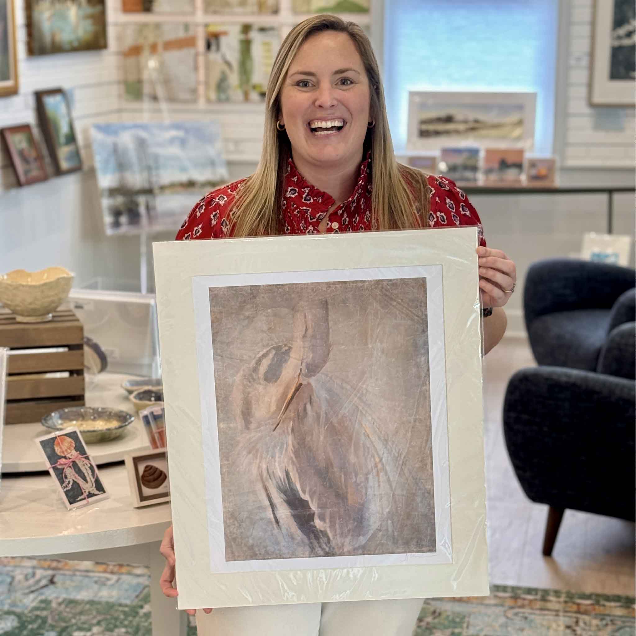 Bordy holding Phoenix Rising great blue heron fine art giclée print by Helli Luck inside Gray Man Gallery Pawleys Island showing artwork scale and wildlife art presentation