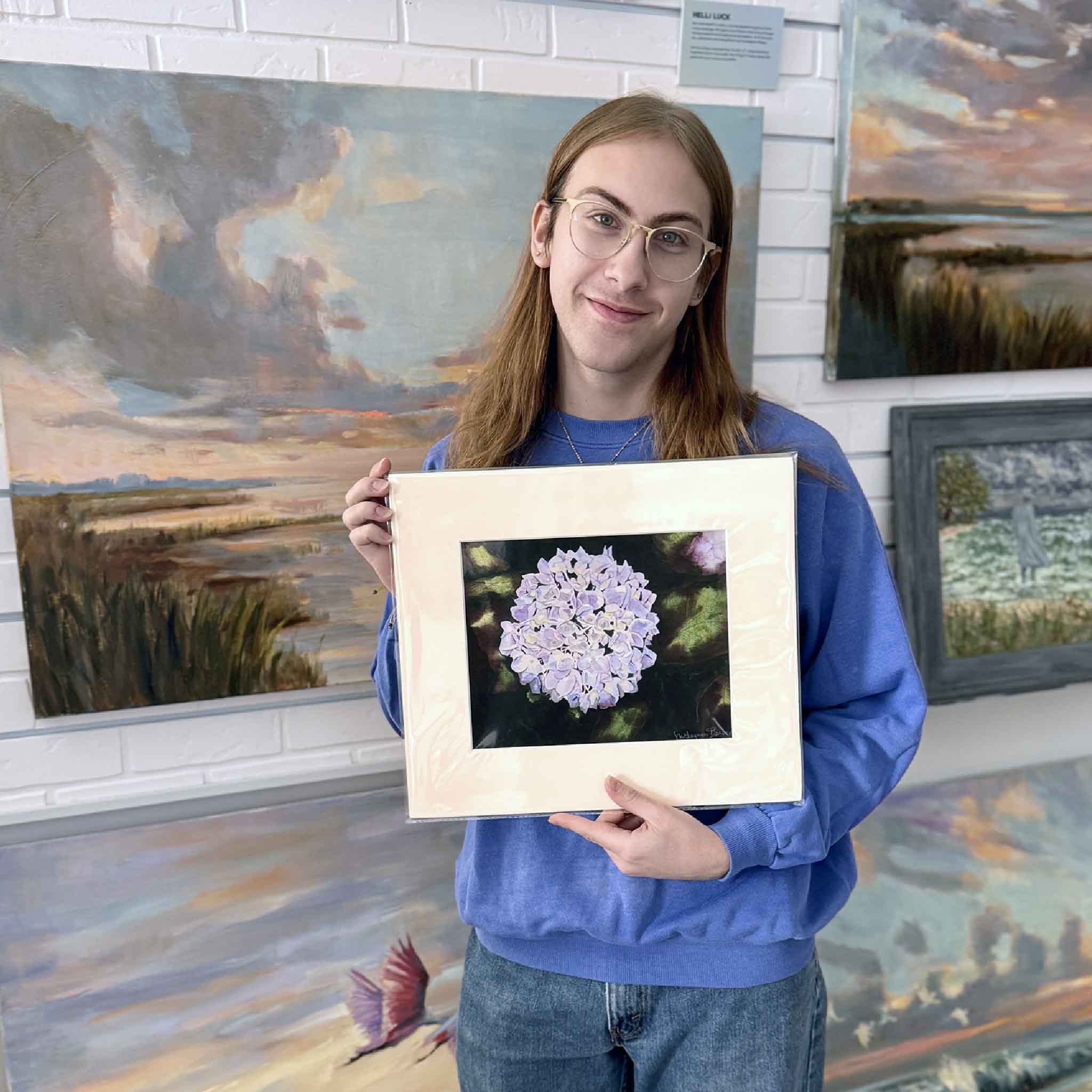 A Gray Man Gallery team member holds Hydrangea 7 by Mimi Beaver, an original watercolor featuring a pale lavender hydrangea bloom against deep green foliage, donated to benefit Salty Dogs Senior Animal Rescue.