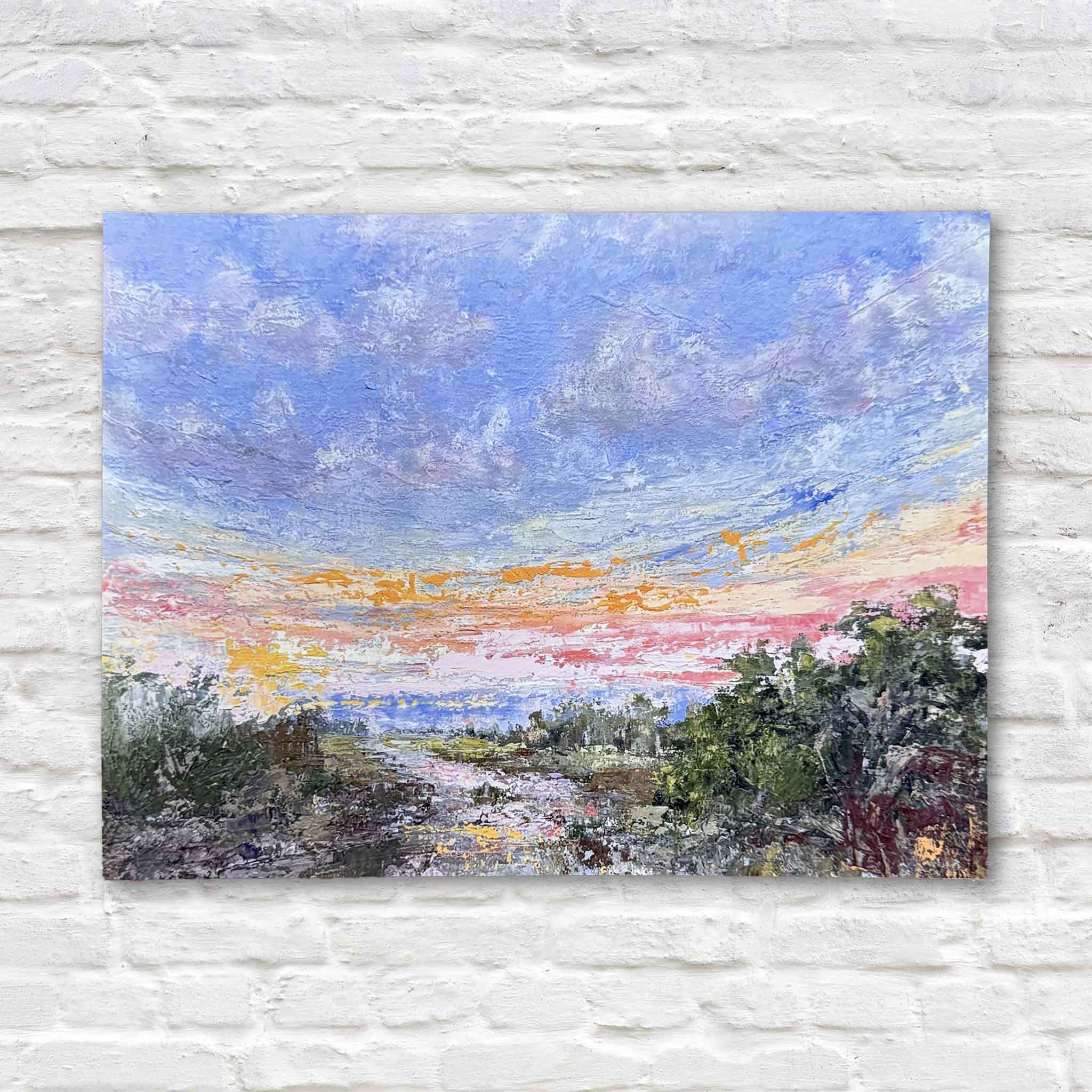 Unmatted 9x12 fine art giclée print of Marshlight by local artist Jeanne O’Neal displayed against a white brick wall at Gray Man Gallery in Pawleys Island, featuring an expansive Lowcountry marsh sunset with layered brushwork, luminous sky tones, and expressive texture reproduced with archival quality inks